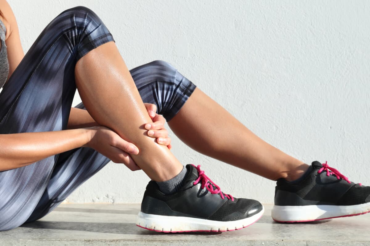 Running sport injury leg pain – runner woman runner hurting holding painful sprained ankle muscle.