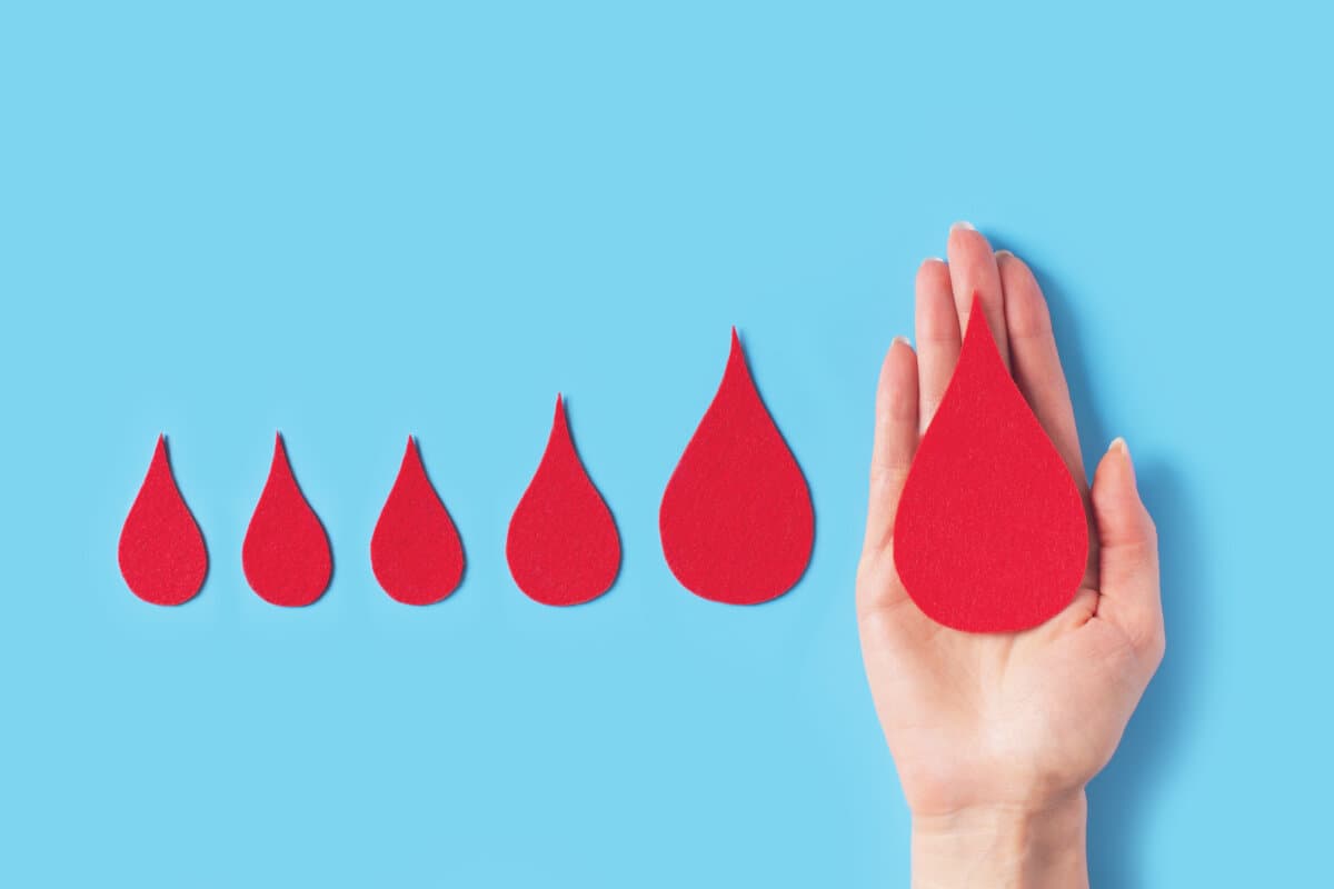 World hemophilia day concept with red blood drop simbol and hands on blue background, copy space, top view