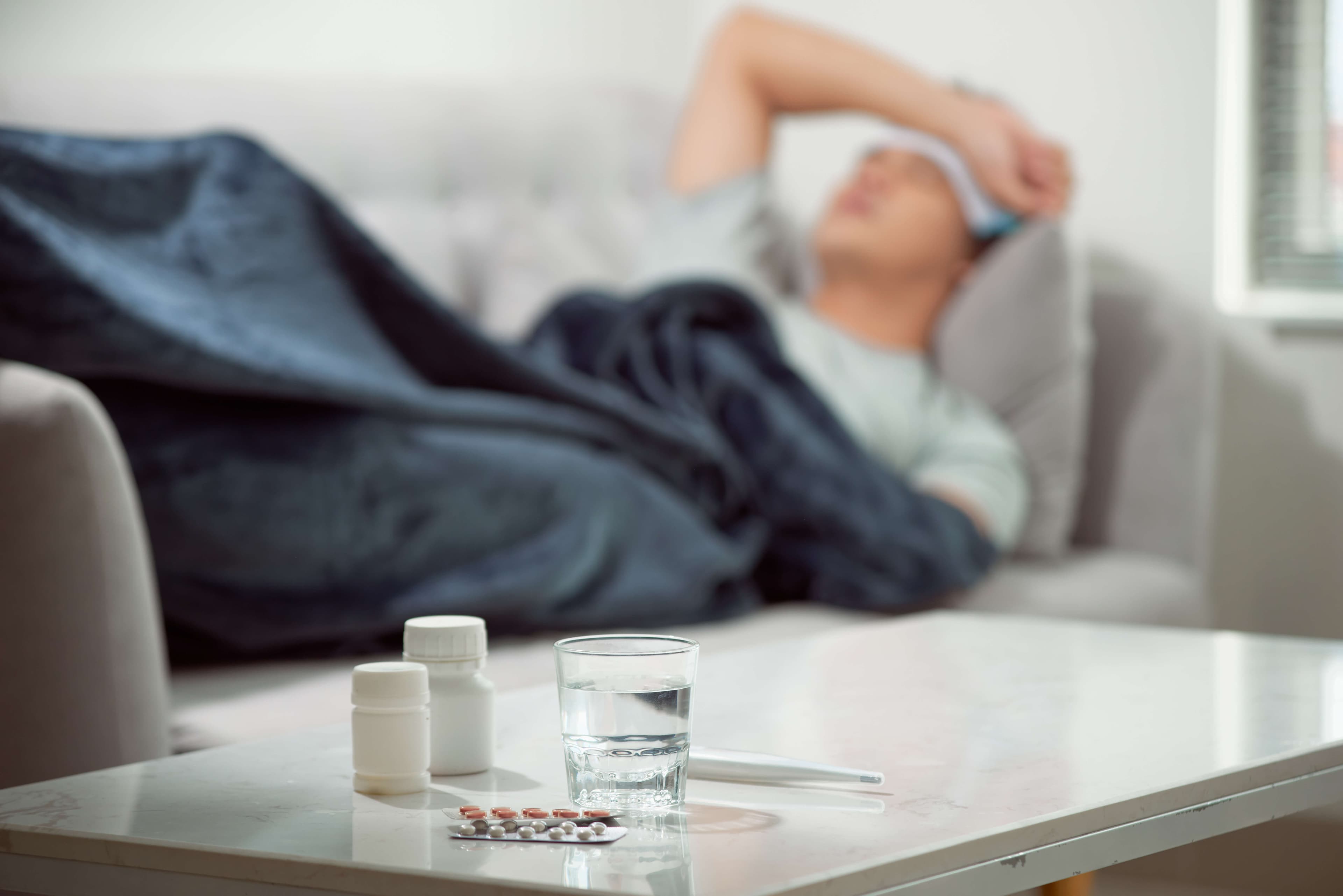 sick wasted man lying in sofa suffering cold and winter flu virus having medicine tablets in health care concept looking
