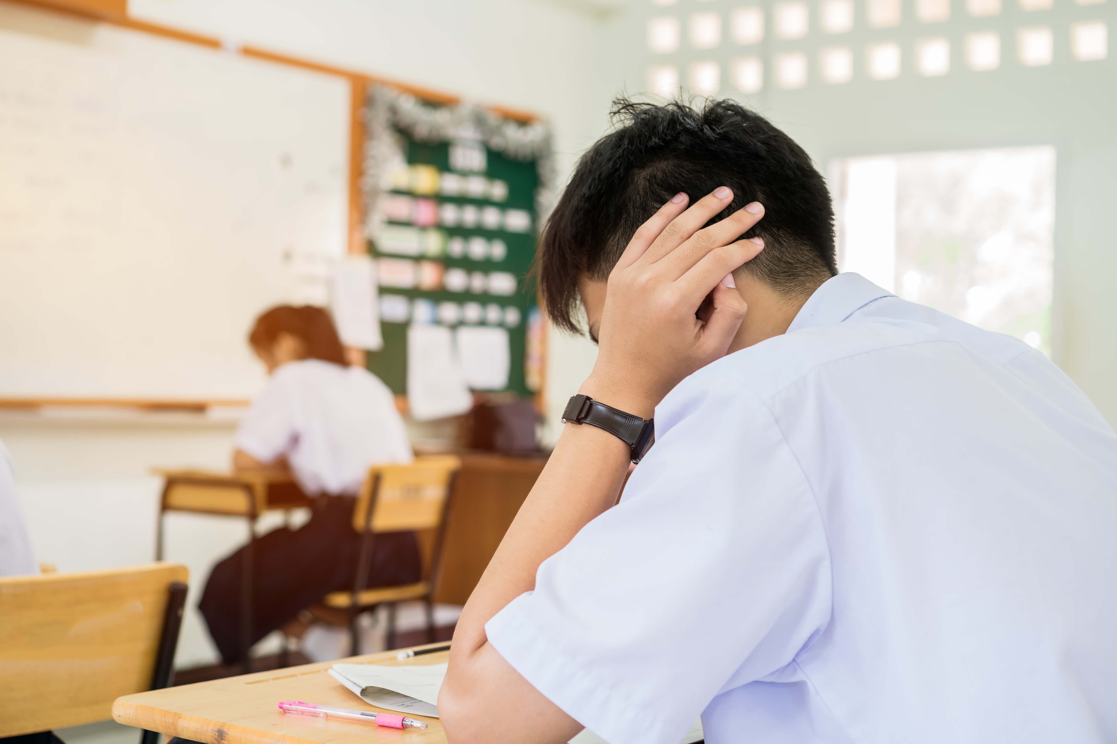 stressed headaches, Asian boy student studying for test or exams in classroom, learning lessons doing final exam at high