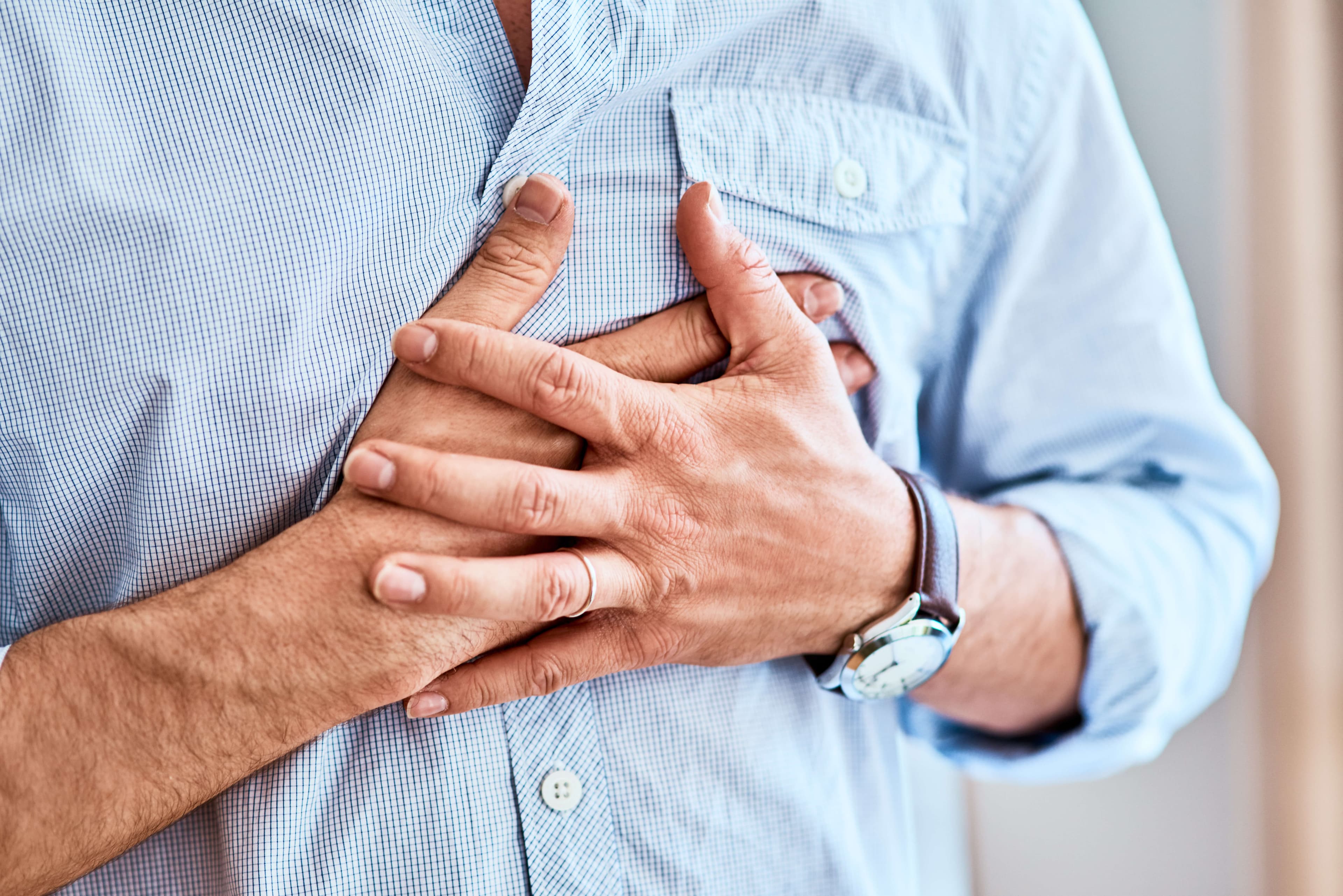 Shot of a unrecognizable man holding his chest in discomfort due to pain at home during the day.