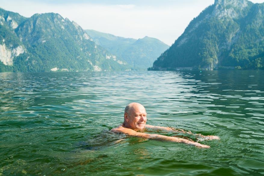 Senior im See am baden im Hintergrund sind Berge zu sehen
