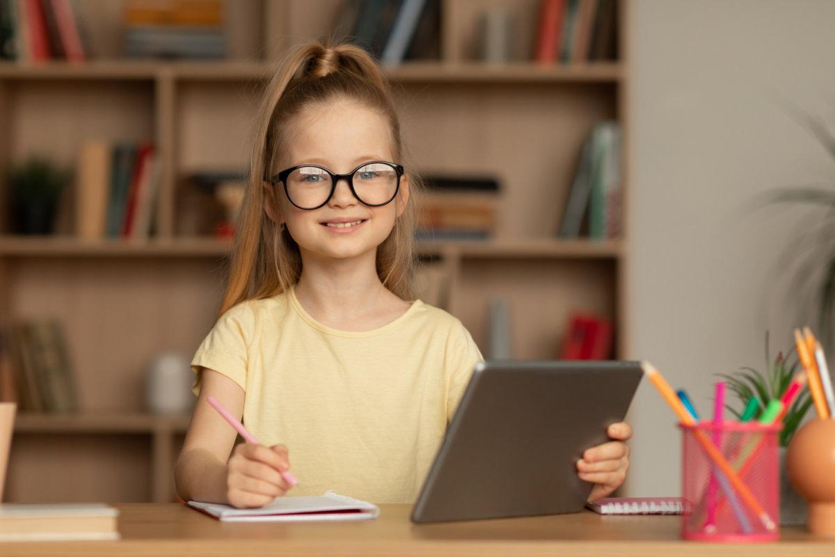 Schulmädchen macht sich Notizen mit einem digitalen Tablet und posiert drinnen sitzend