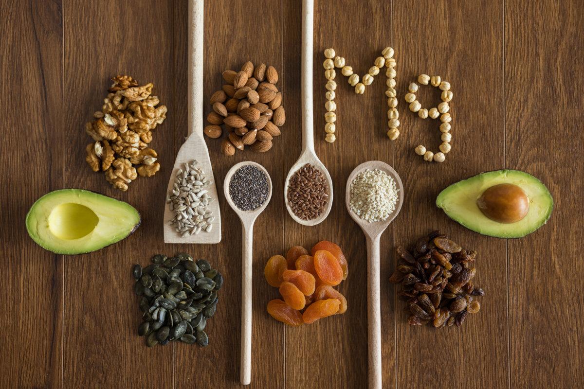 Holzlöffel mit gesunden Samen, Nüssen und Trockenfrüchten und Wort Mg auf Holztisch angeordnet