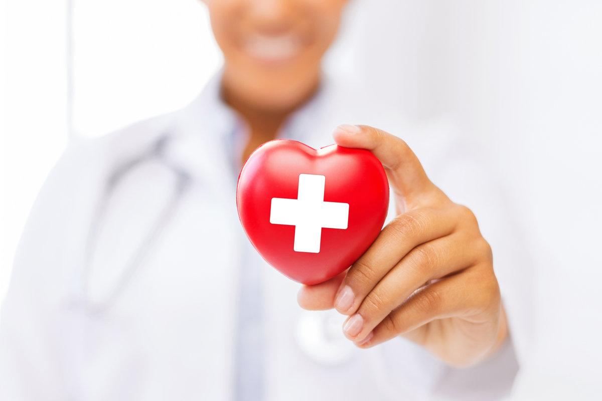 Gesundheits- und Medizinkonzept - afroamerikanische Ärztin hält Herz mit rotem Kreuzsymbol