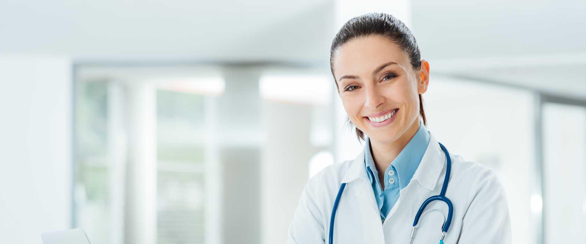 Zuversichtlich Ärztin, die am Schreibtisch sitzt und an Kamera-, Gesundheits- und Präventionskonzept lächelt
