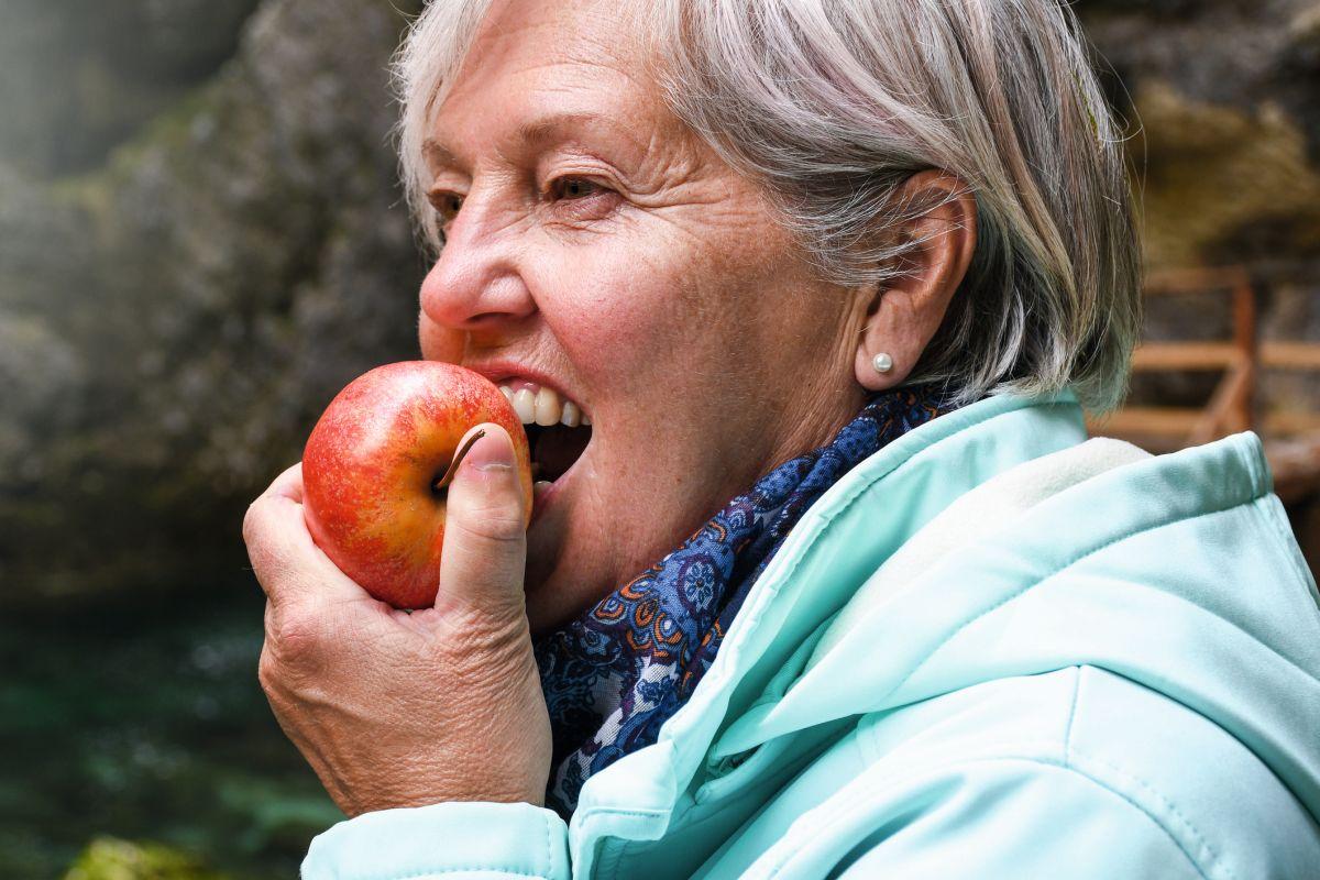 Gesund aussehende ältere Frau mit grauem Haar, das Apfel draußen im Park isst