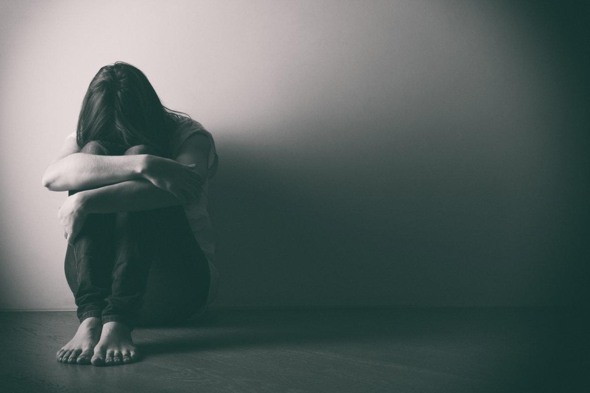 Teenager-Mädchen mit Depressionen sitzt allein auf dem Boden im dunklen Raum. . Schwarz-Weiß-Foto
