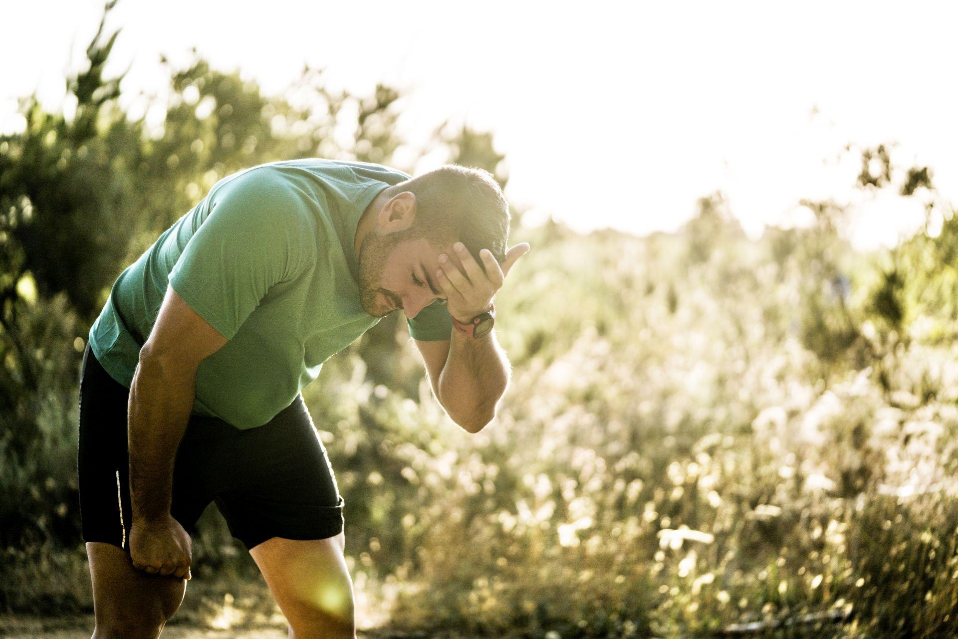Müder männlicher Jogger, der im Wald biegt. Mittlerer erwachsener Mann ist in Sportkleidung. Er trainiert an einem sonnigen Tag im Wald.