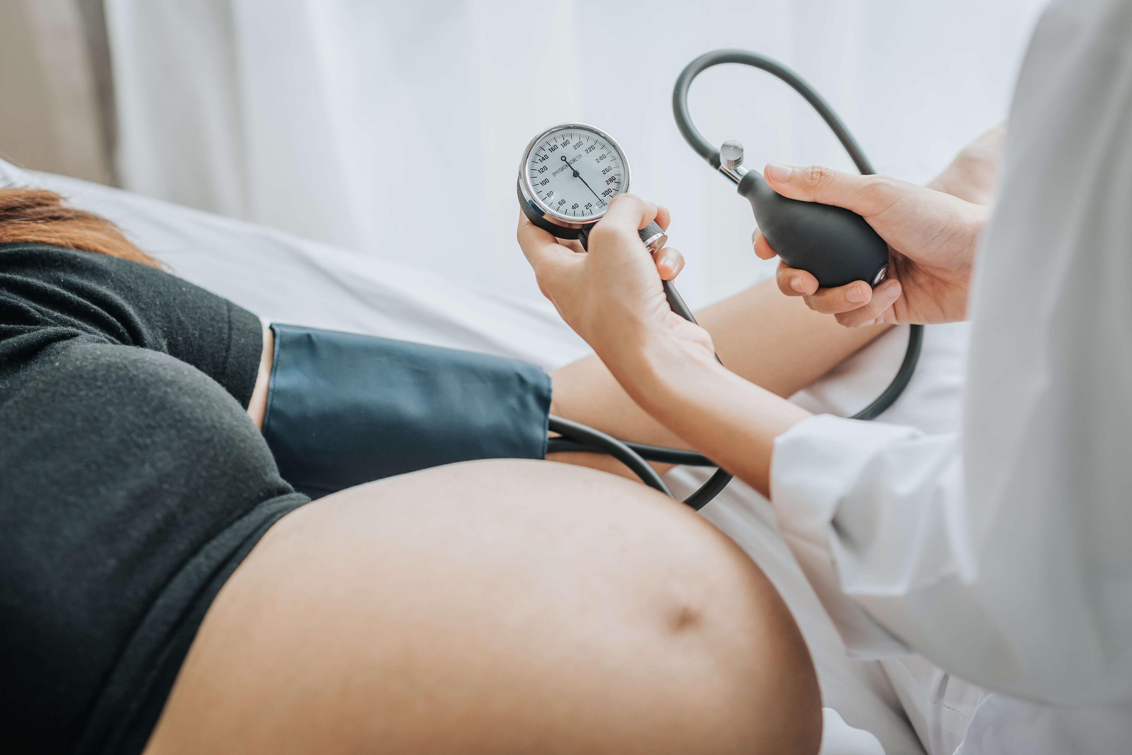 Arzt, der den Blutdruck einer schwangeren Patientin mit Blutdruckmessgerät im Bett prüft