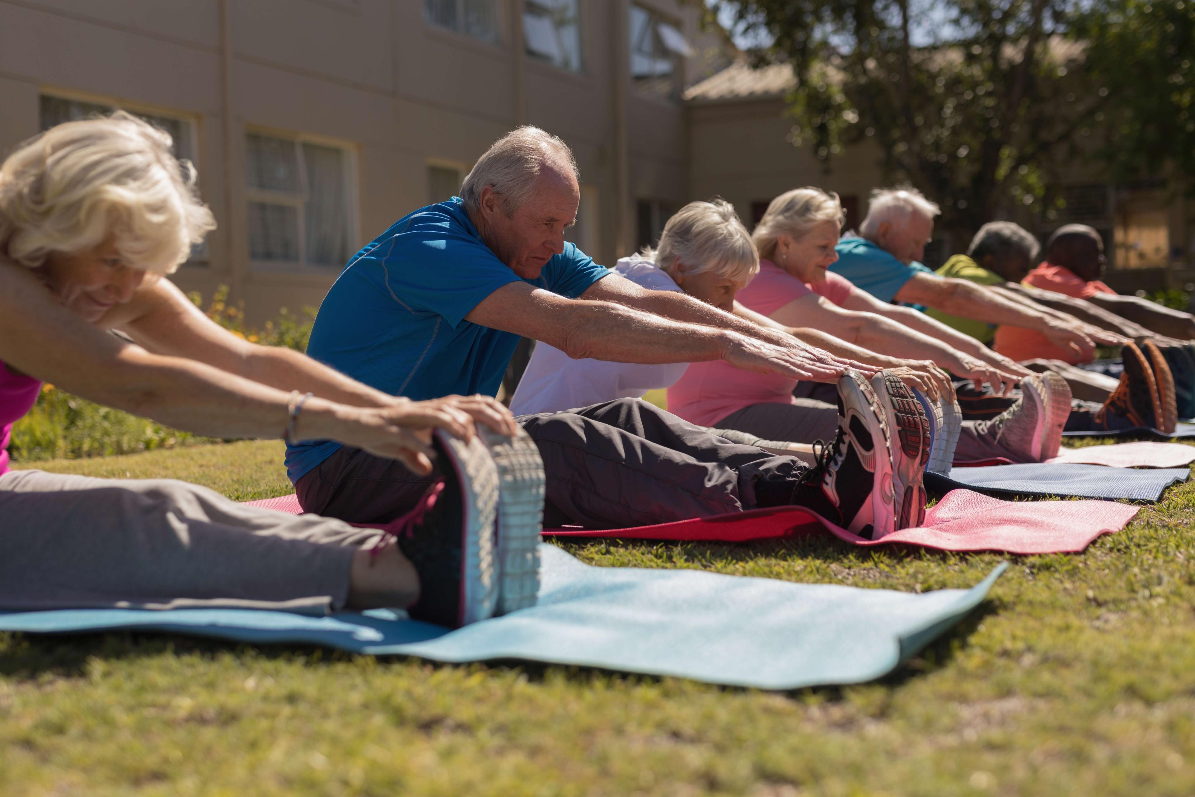 Seitenansicht der Gruppe der aktiven älteren Leute, die ihre Beine auf der Yogamatte im Park trainieren und kratzen