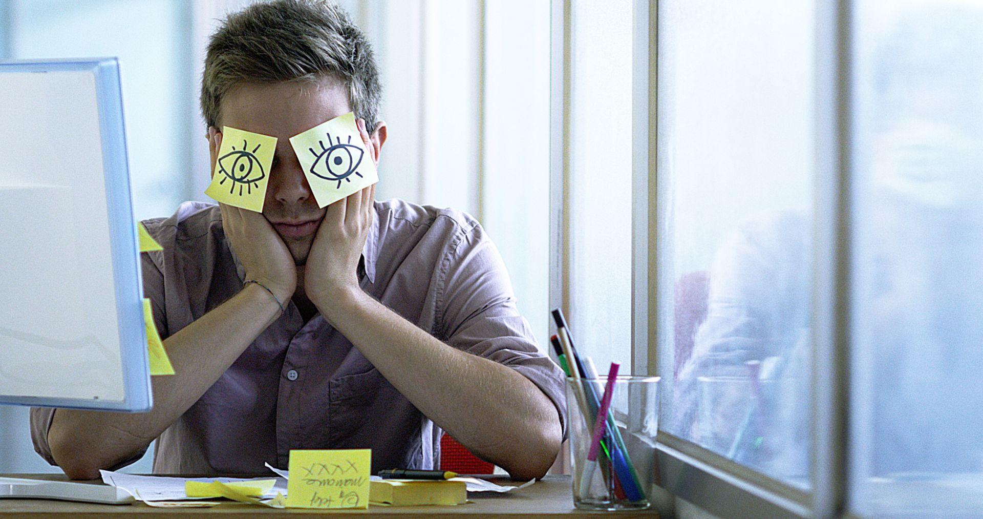 Ein junger Angestellter schläft im Büro und versteckt sich mit Posits in den Augen