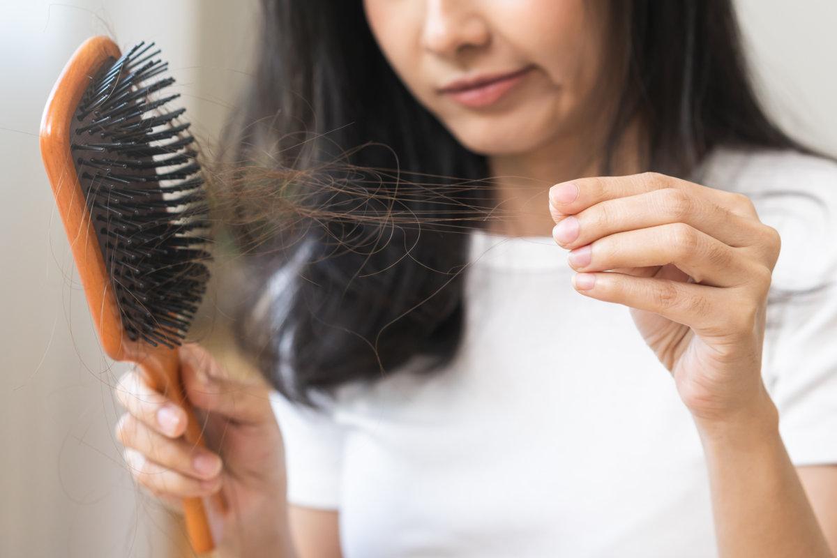 Ernsthafte asiatische junge Frau mit Bürste, Kamm und Haarbürste, nach dem Bürsten fielen schwarze Haare von der Kopfhaut