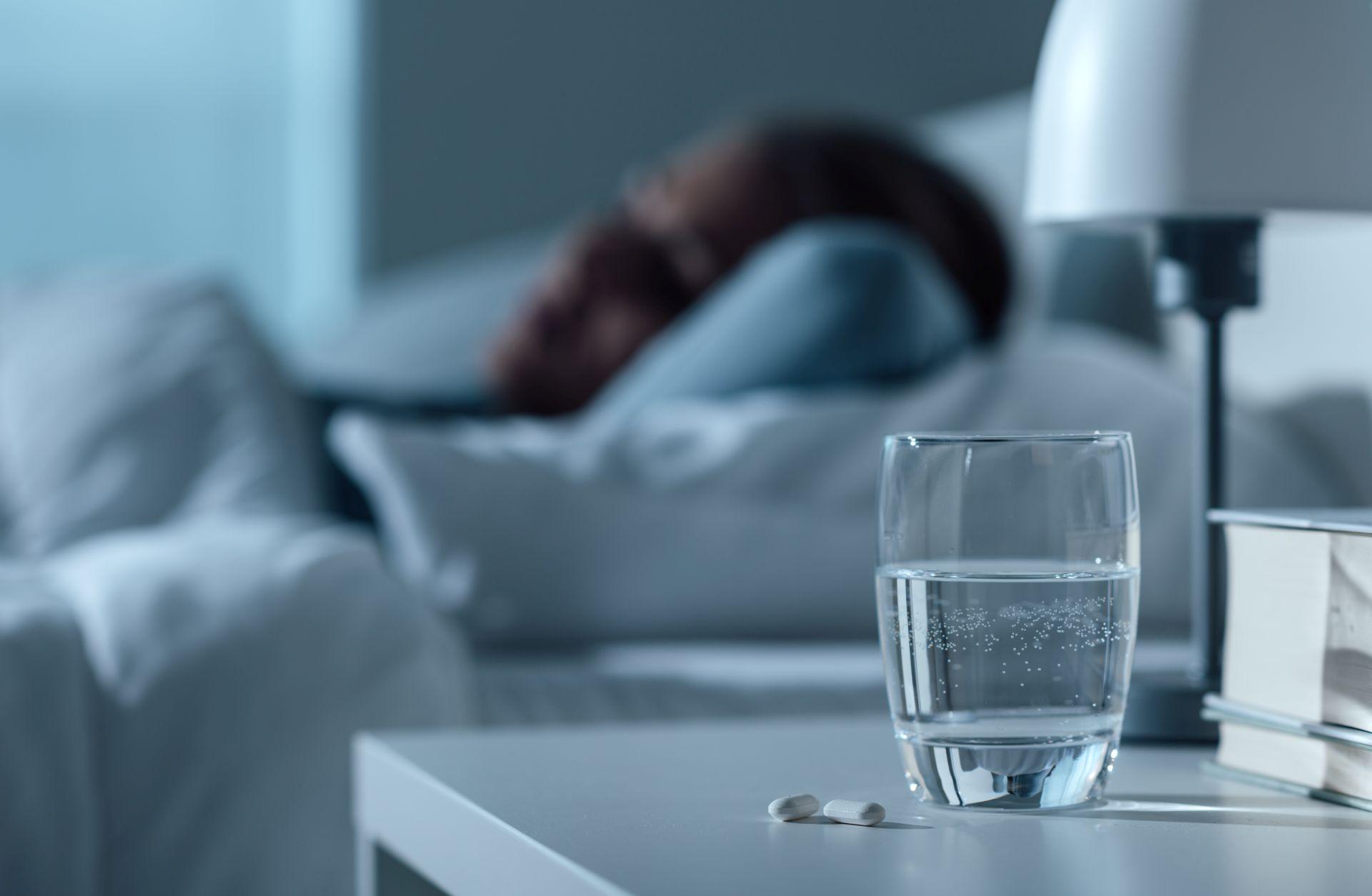 Frau, die in ihrem Bett nachts schläft, Glas auf Wasser und Pillen auf dem Vordergrund, Medizin- und Behandlungskonzept