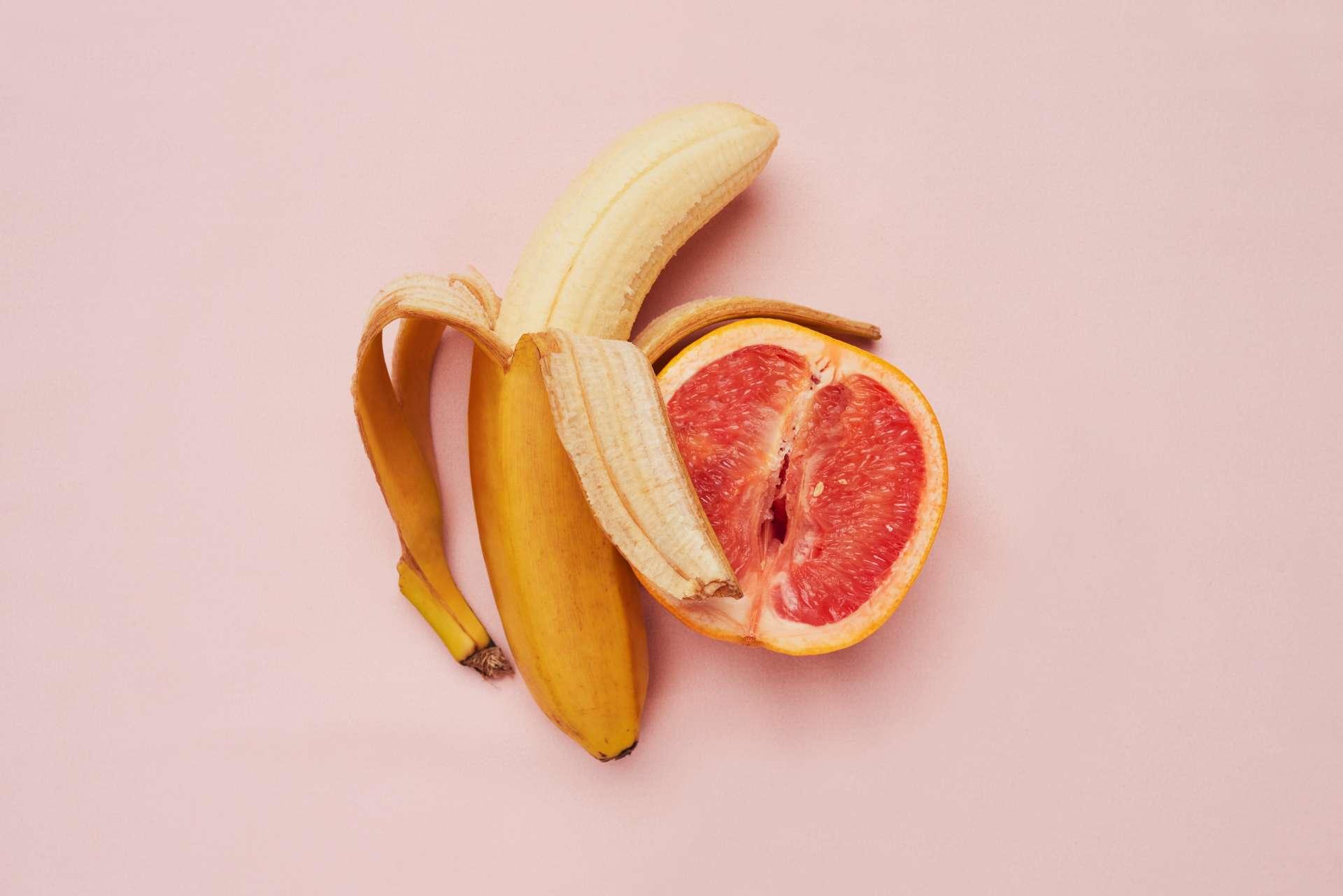 Studioaufnahme einer Banane und Grapefruit in einer suggestiven Position vor einem rosa Hintergrund