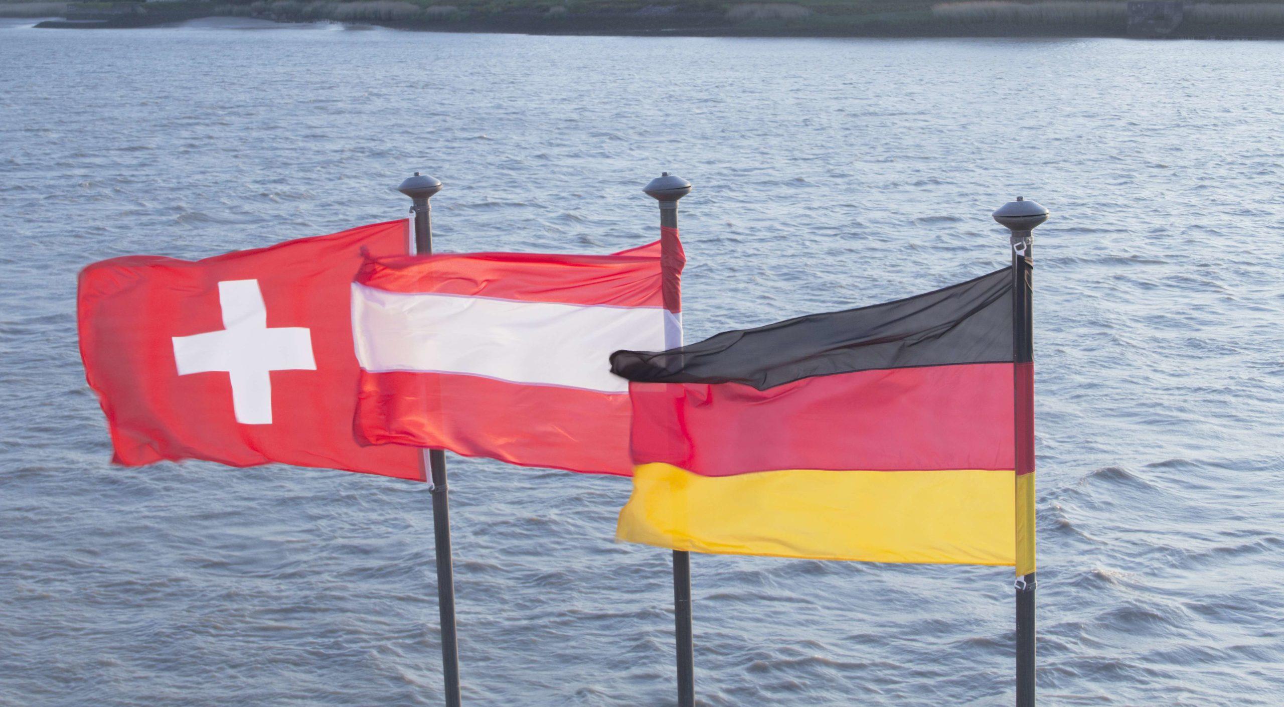 Eine Schweizer, österreichische und deutsche Flagge am Flussufer
