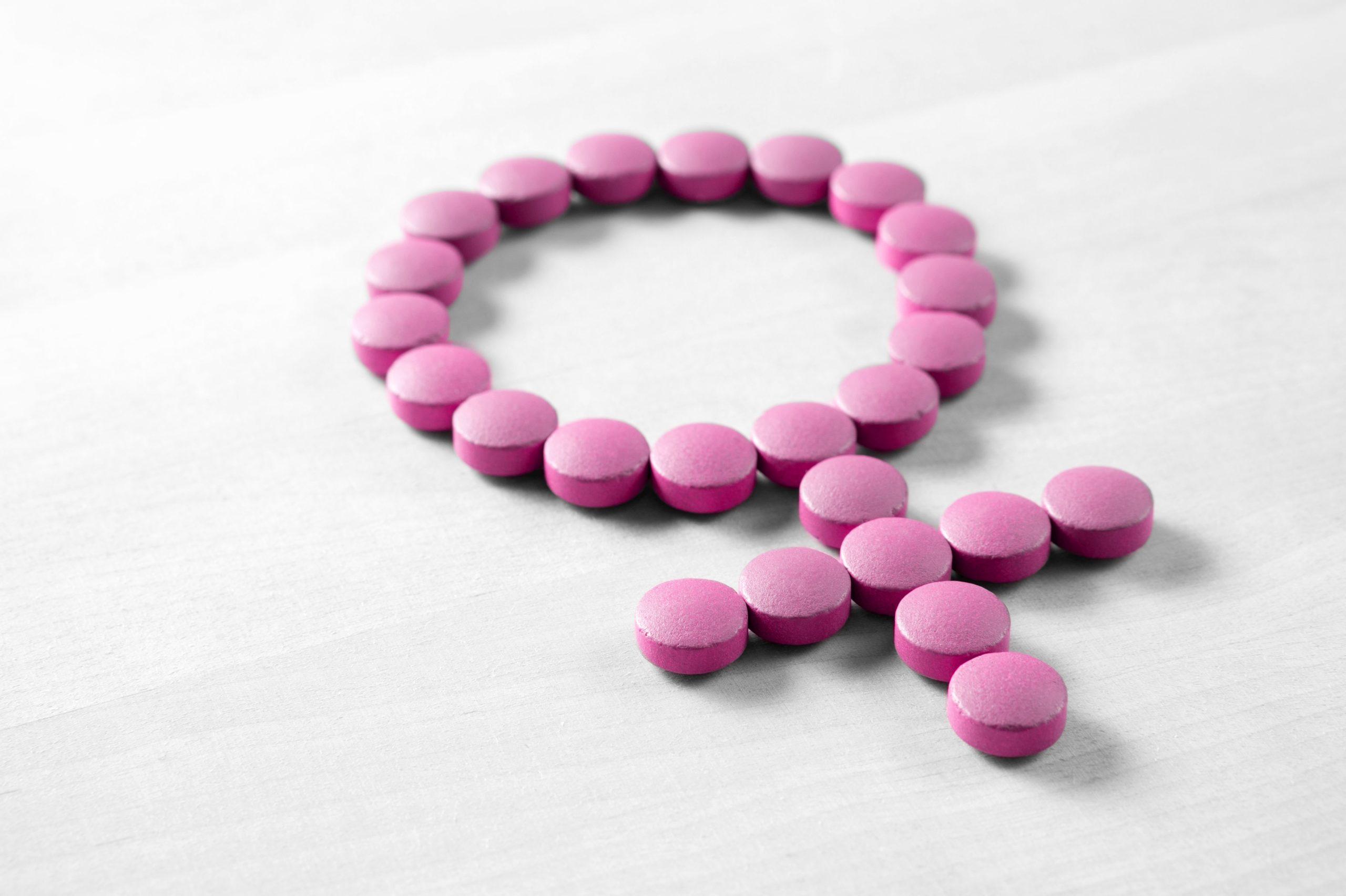 Weibliche Gesundheit. Geschlechtssymbol aus rosaroten Pillen oder Tabletten auf Holztisch