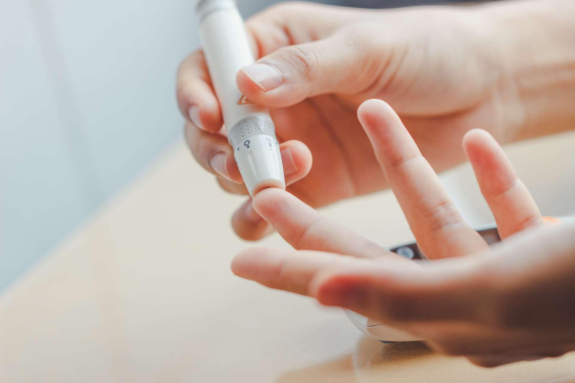 Nahaufnahme von Frauenhänden mit Lanzette am Finger, um den Blutzuckerspiegel mit dem Glukosemeter zu überprüfen, das als Medizin verwendet wird