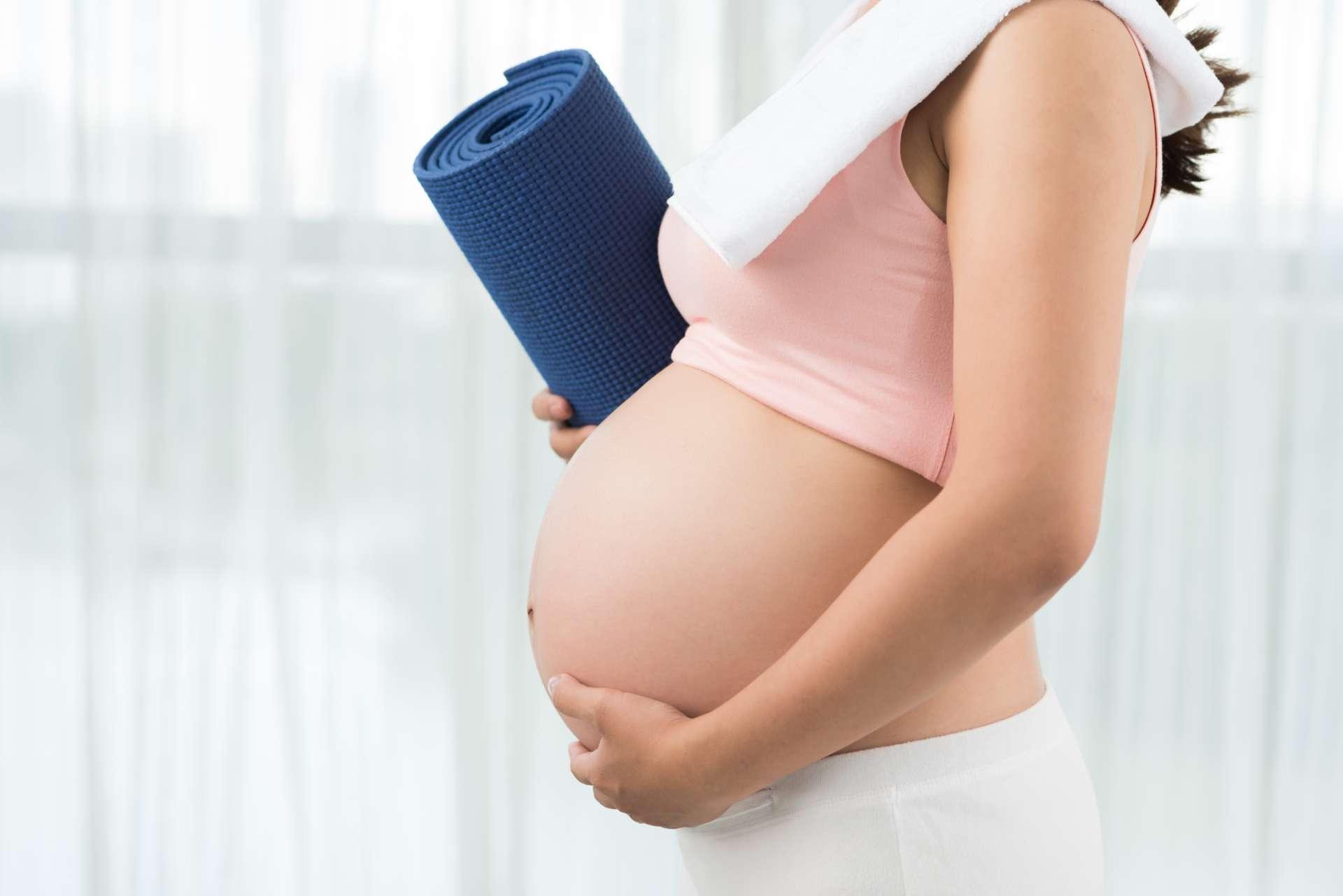 Abgeschnittenes Bild einer sportlichen schwangeren Frau mit Yogamatte