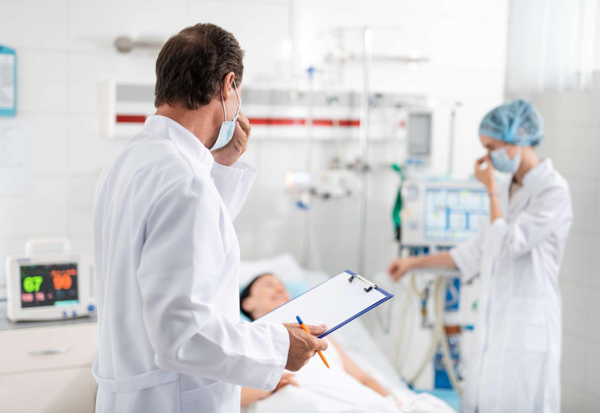 Doktor mit der medizinischen Form in der Hand, die Krankenschwester betrachtet, die nahe Patient steht