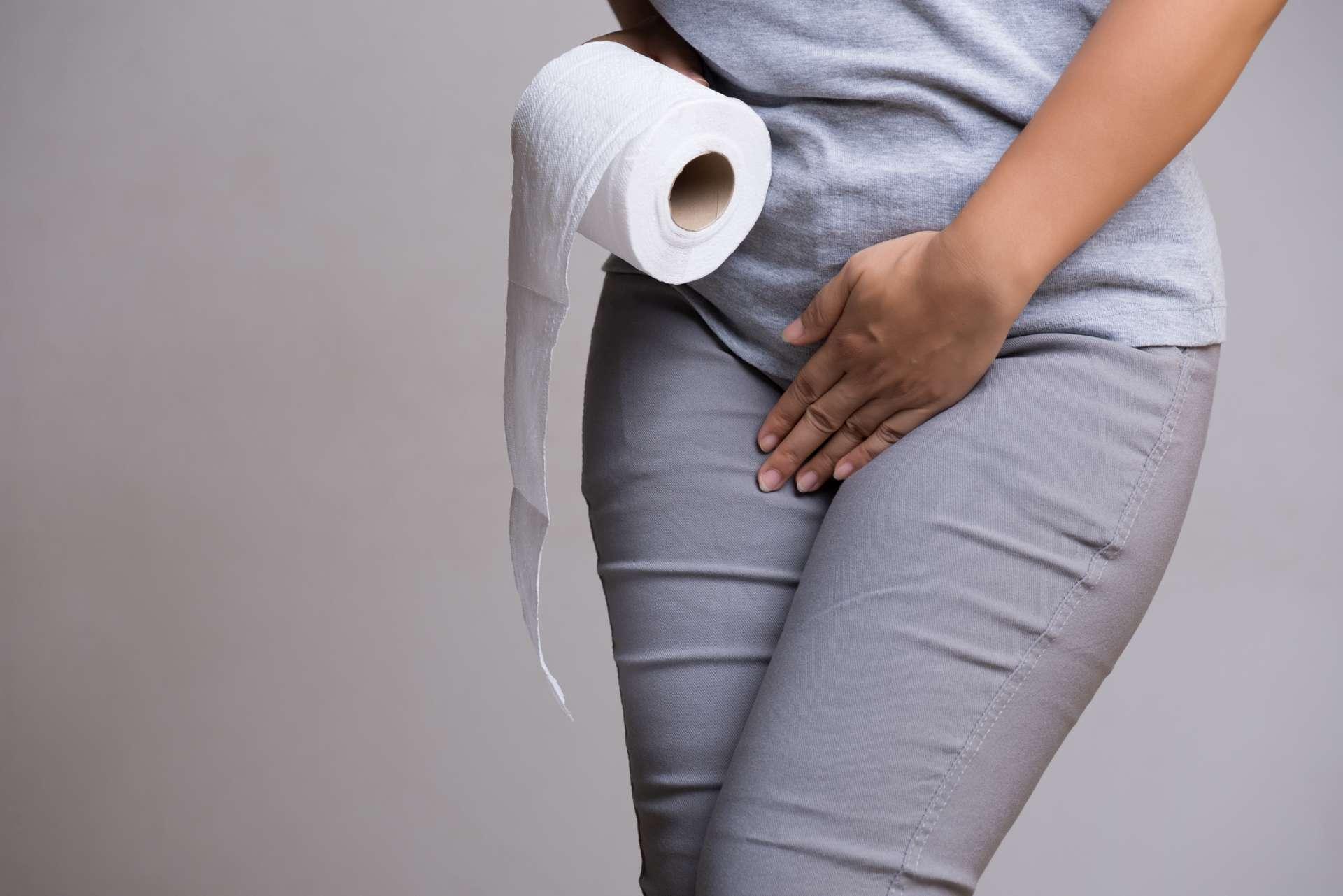 Frauenhand, die ihren Unterbauch im Schritt und Gewebe- oder Toilettenpapierrolle hält. Störung, Durchfall, Inkontinenz. Gesundheitskonzept.