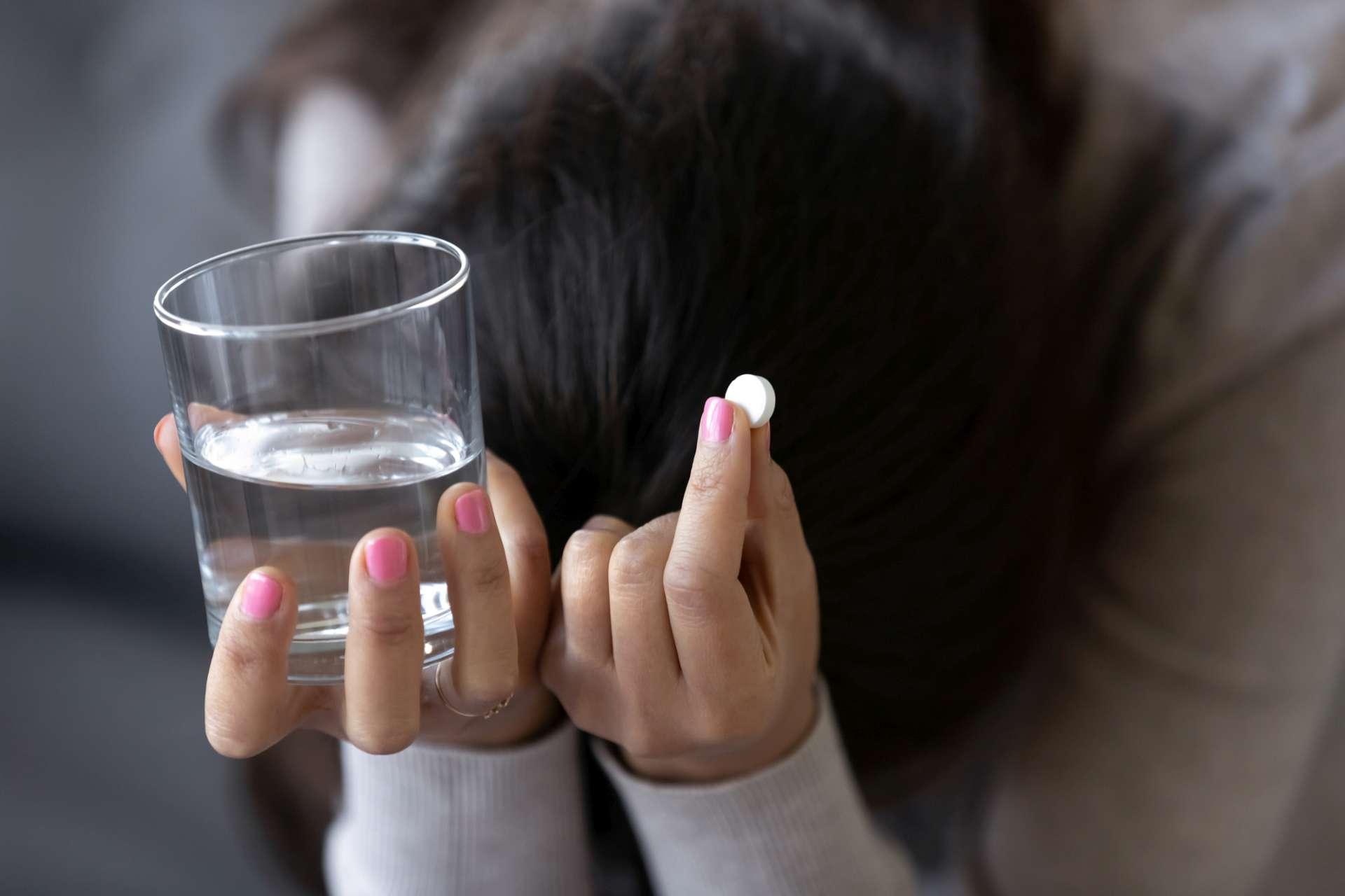 Traurige depressive Frau, die Pille und Glas Wasser hält
