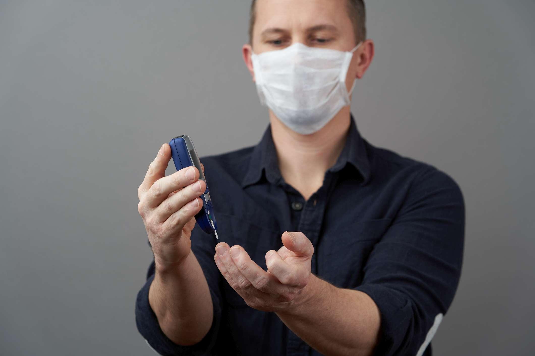 Mann, der Blutzuckerspiegel mit Glukometer auf grauem Hintergrund prüft