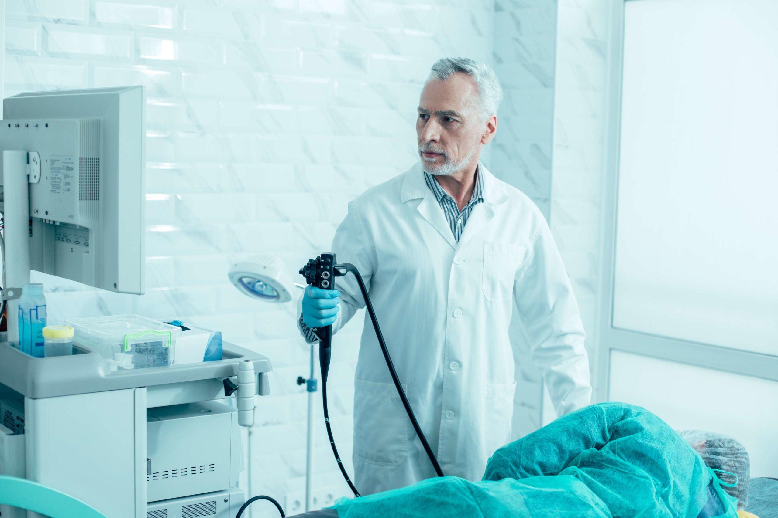 Ernsthafter reifer Arzt, der ein modernes Endoskop hält und sich auf das Verfahren vorbereitet