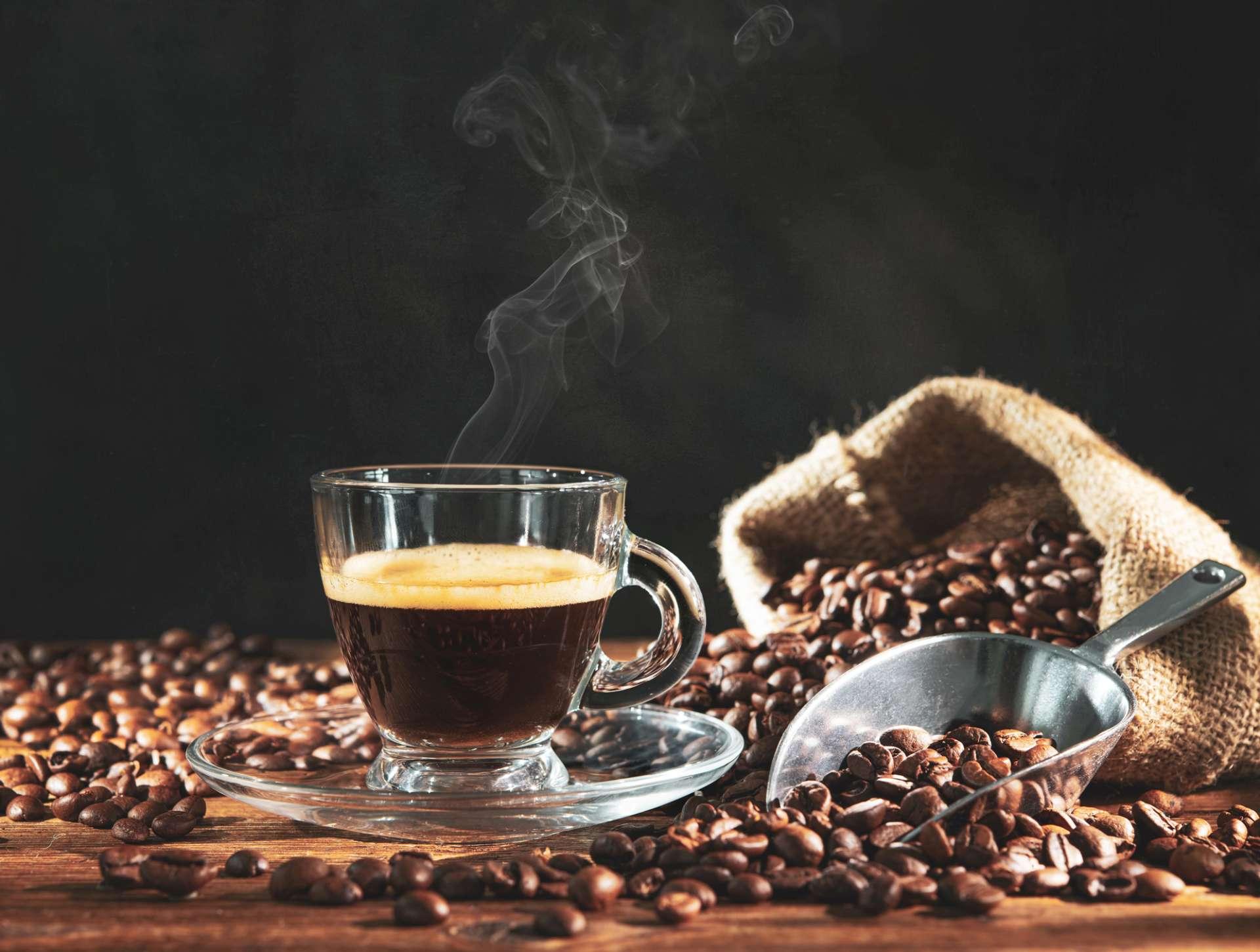 Tasse Espresso mit Kaffeebohnen, Tasche, Schaufel und Dampf auf dunklem Holzhintergrund