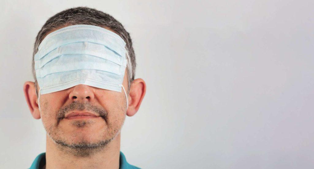 isolierter Mann mit verbundenen Augen mit chirurgischer Maske über den Augen und nacktem Mund und Nase