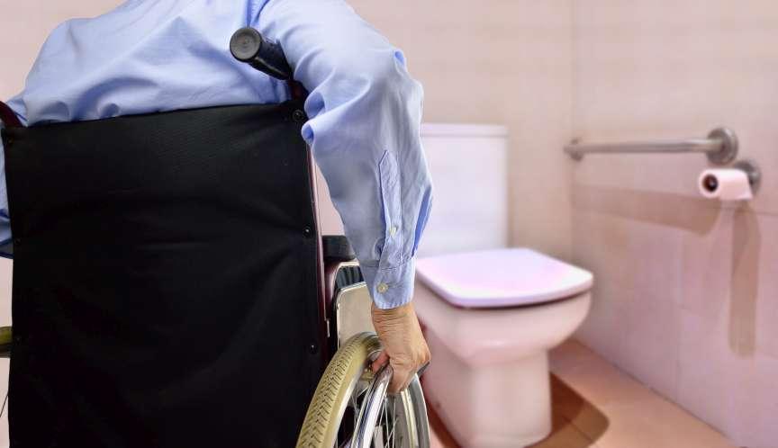 Rückansicht des Mannes im Rollstuhl, der zur Toilette geht, angepasst für behinderte Person