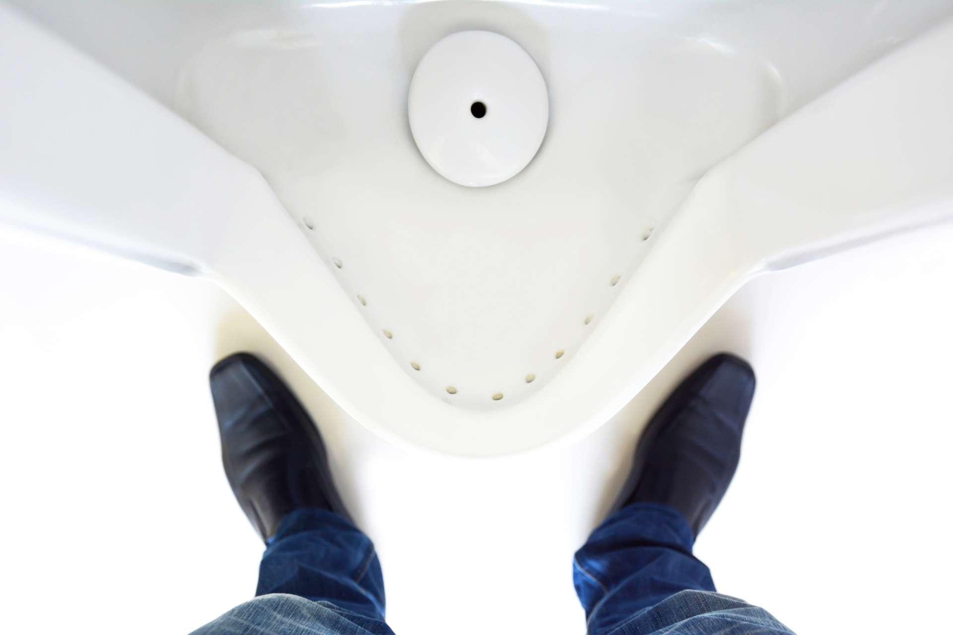 Draufsicht auf die Beine eines Mannes vor dem Urinal in der Herrentoilette
