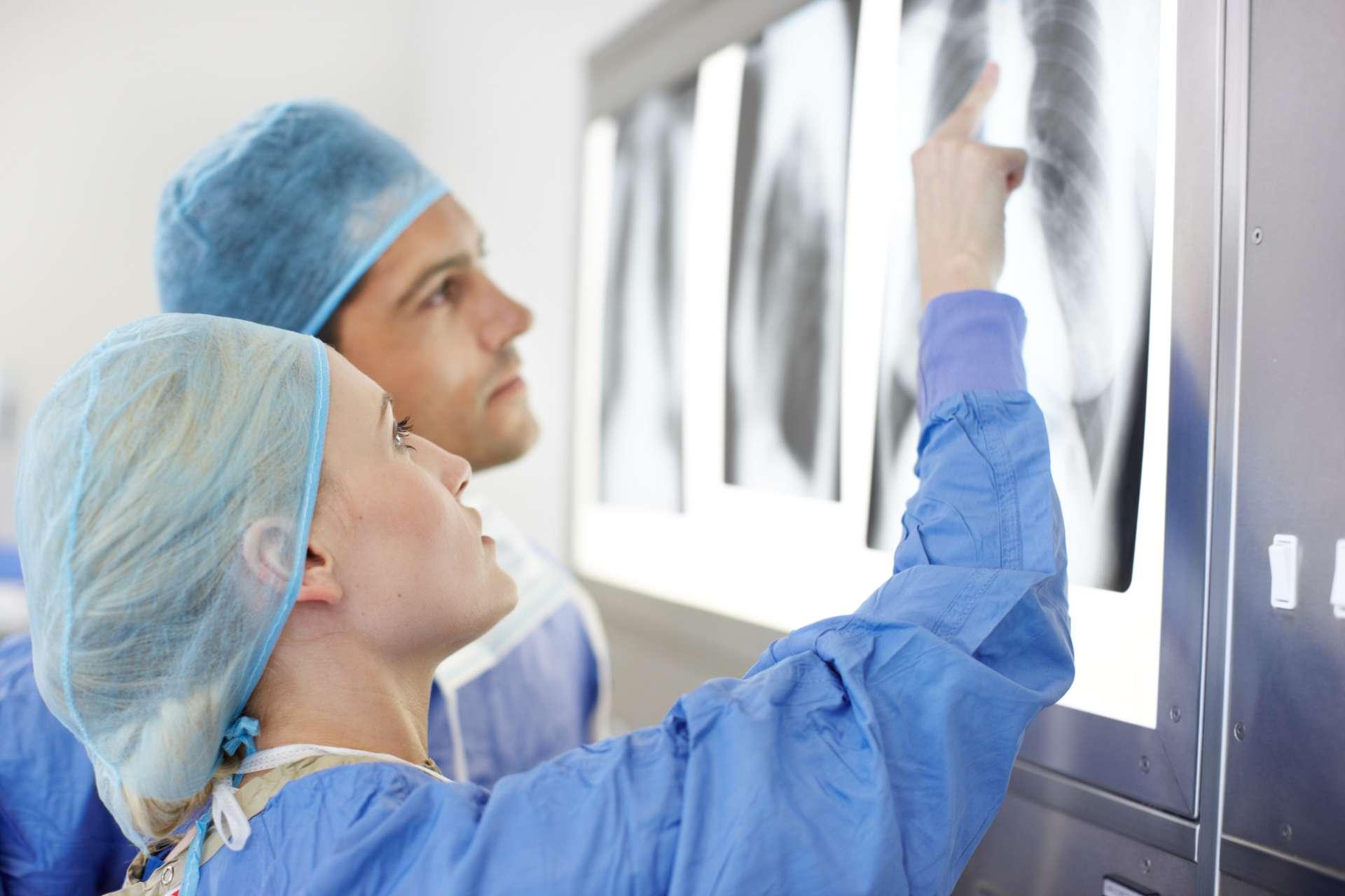 Profil einer Ärztin und eines Arztes, die über die Röntgenaufnahmen des Brustkorbs einer Patientin sprechen und darauf zeigen