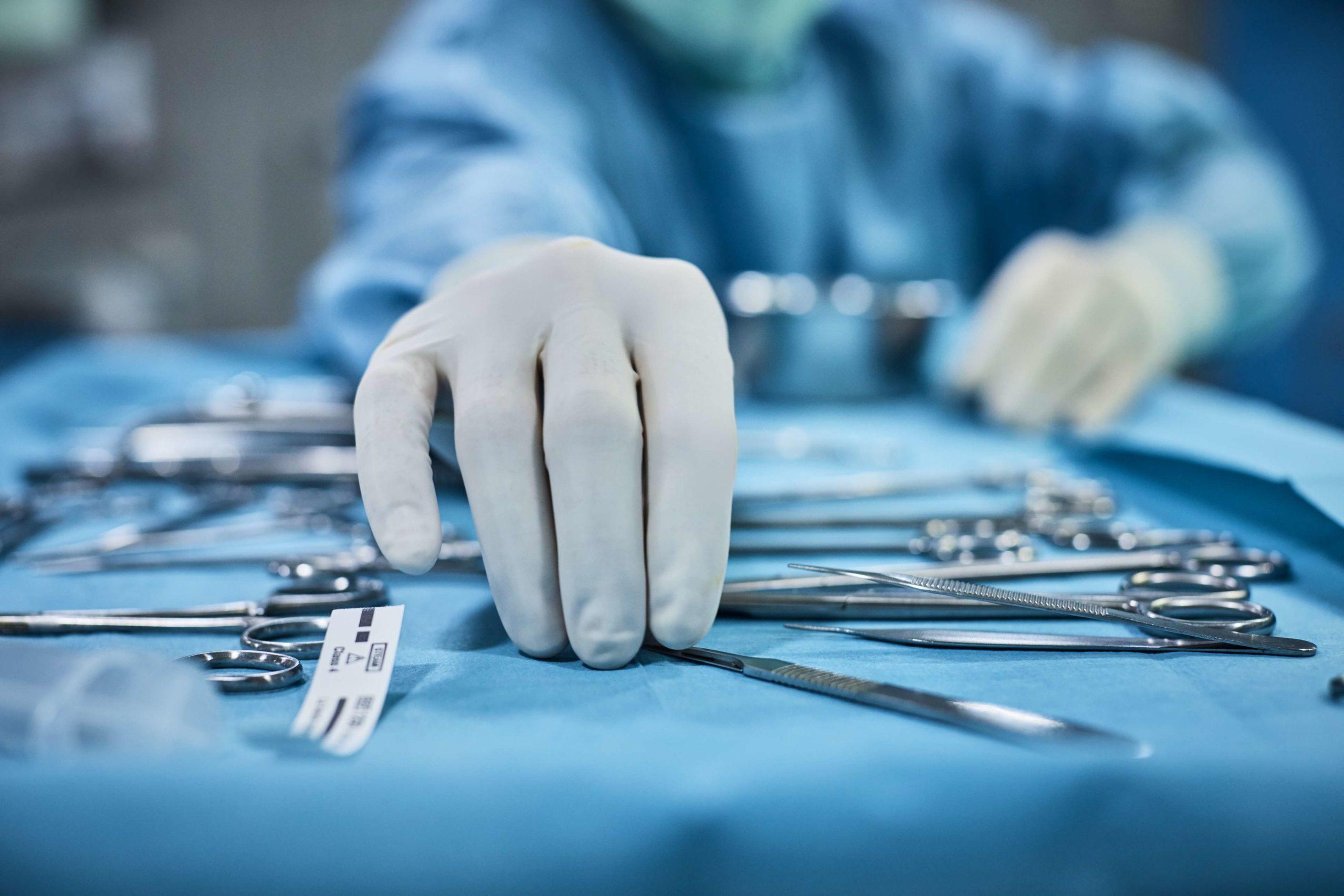 Chirurg nimmt chirurgisches Werkzeug vom Tablett auf. Chirurg bereitet sich im Operationssaal auf die Operation vor. Er befindet sich in einem Krankenhaus.