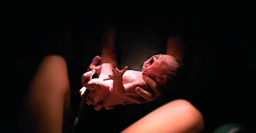 Ein schreiendes Baby wird in beiden Händen gehalten