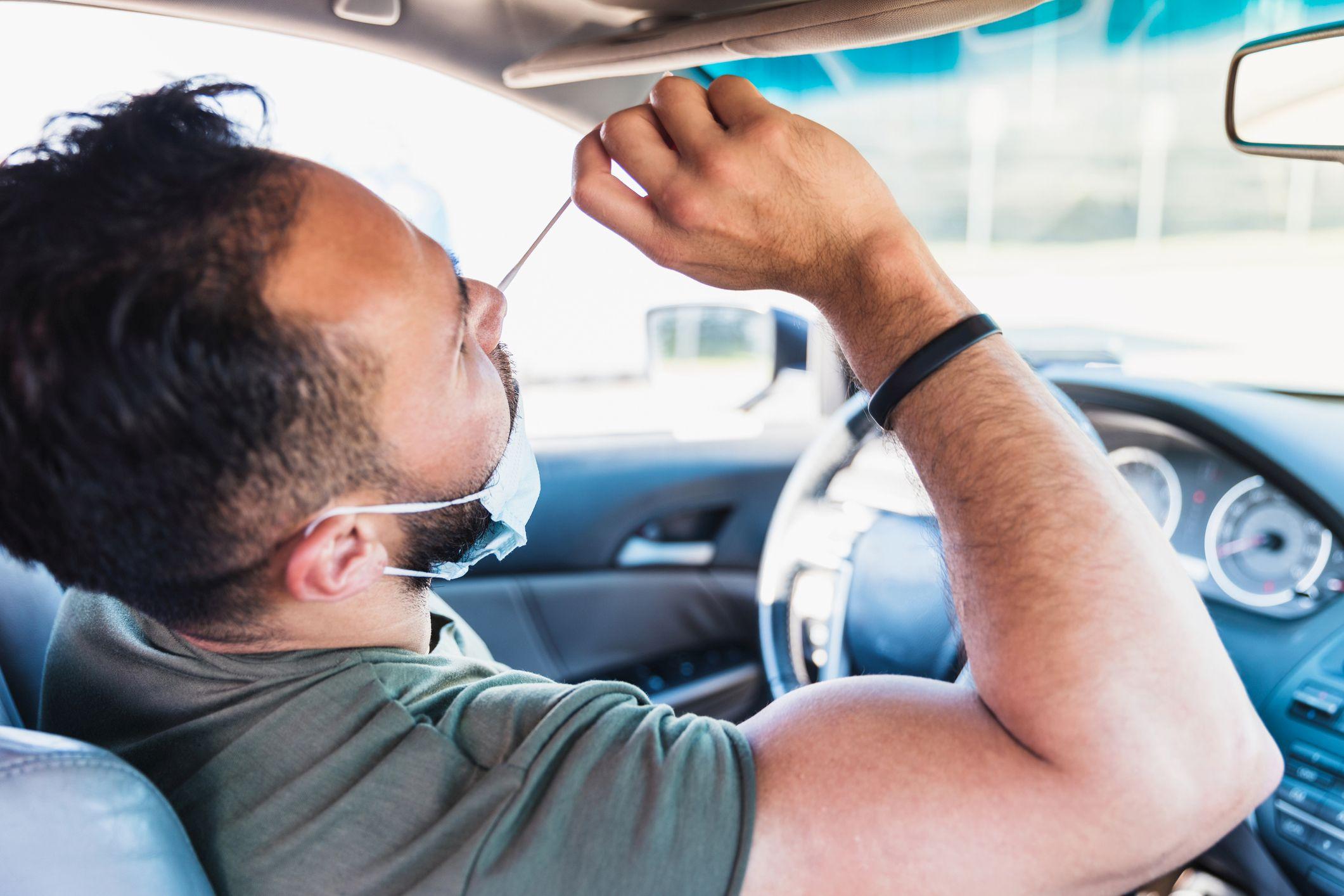 Während er in seinem Auto sitzt, führt ein Mann im mittleren Erwachsenenalter einen Selbst-COVID-Test auf einer Fahrt durch die COVID-Teststelle durch.