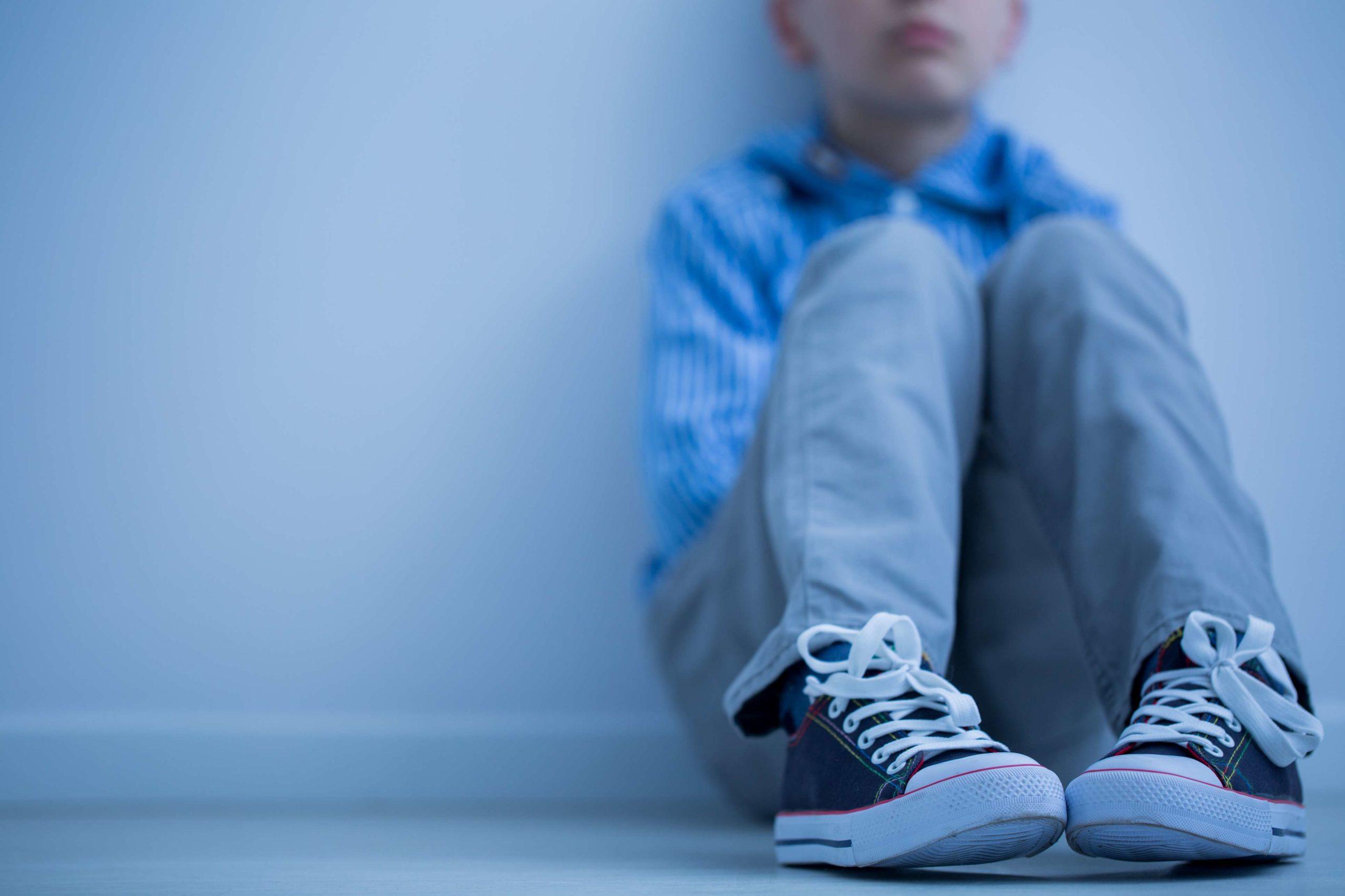 Trauriger Junge in Turnschuhen mit Asperger-Syndrom sitzt alleine in seinem Zimmer