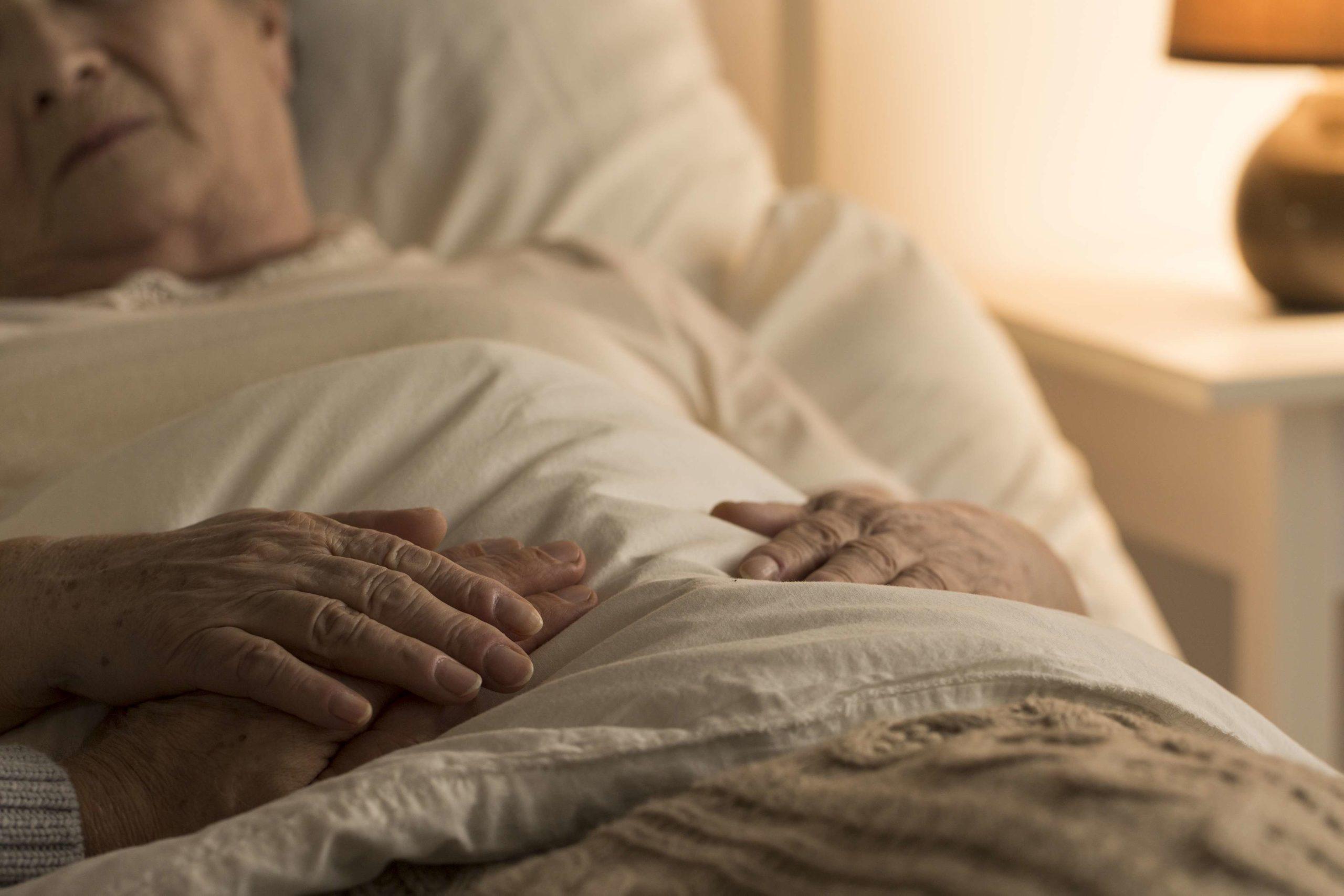Nahaufnahme der Hand des Senioren auf der Hand der sterbenden älteren Person als Zeichen der Unterstützung während der Krankheit