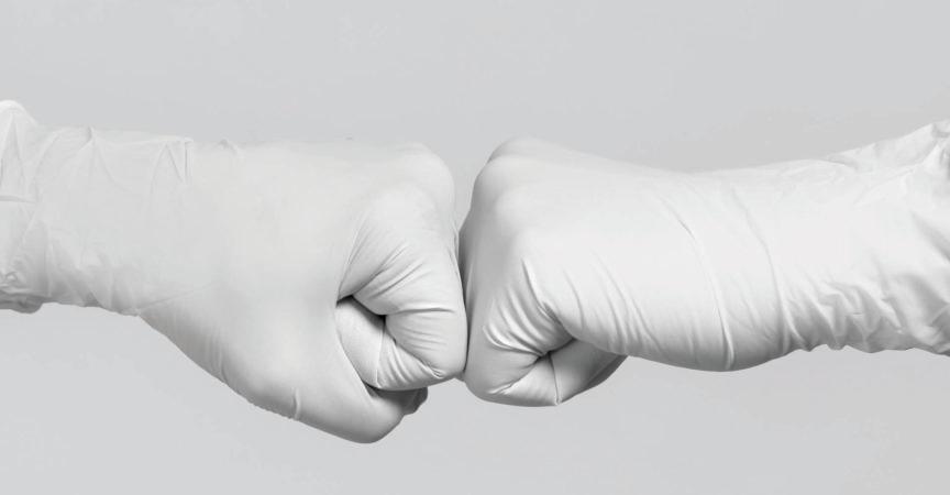 Weiße Handschuhe zum Modell. Kampf gegen das Coronavirus. Zwei medizinische Arbeiter machen eine Fauststoßgeste.