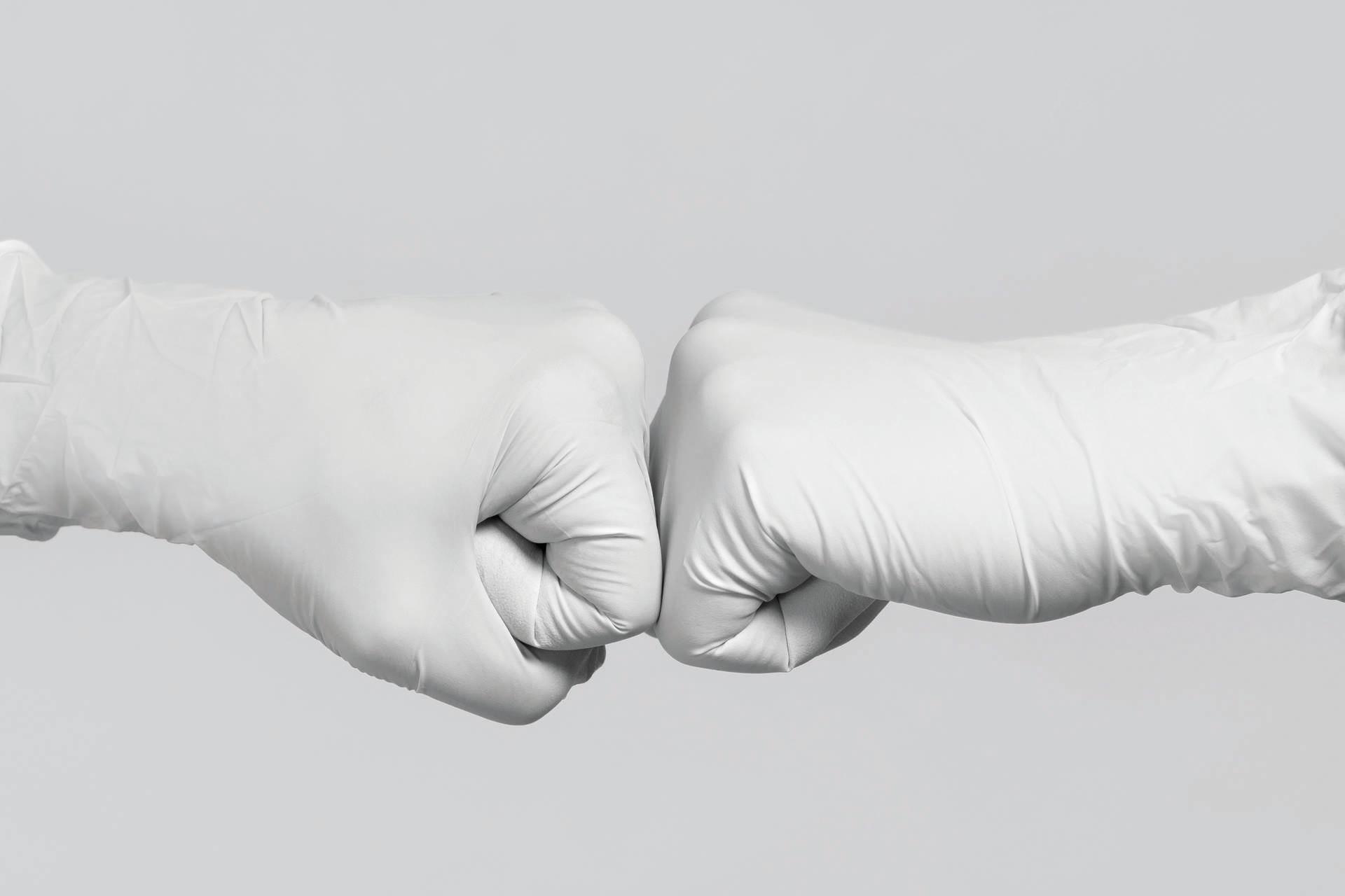 Weiße Handschuhe zum Modell. Kampf gegen das Coronavirus. Zwei medizinische Arbeiter machen eine Fauststoßgeste.
