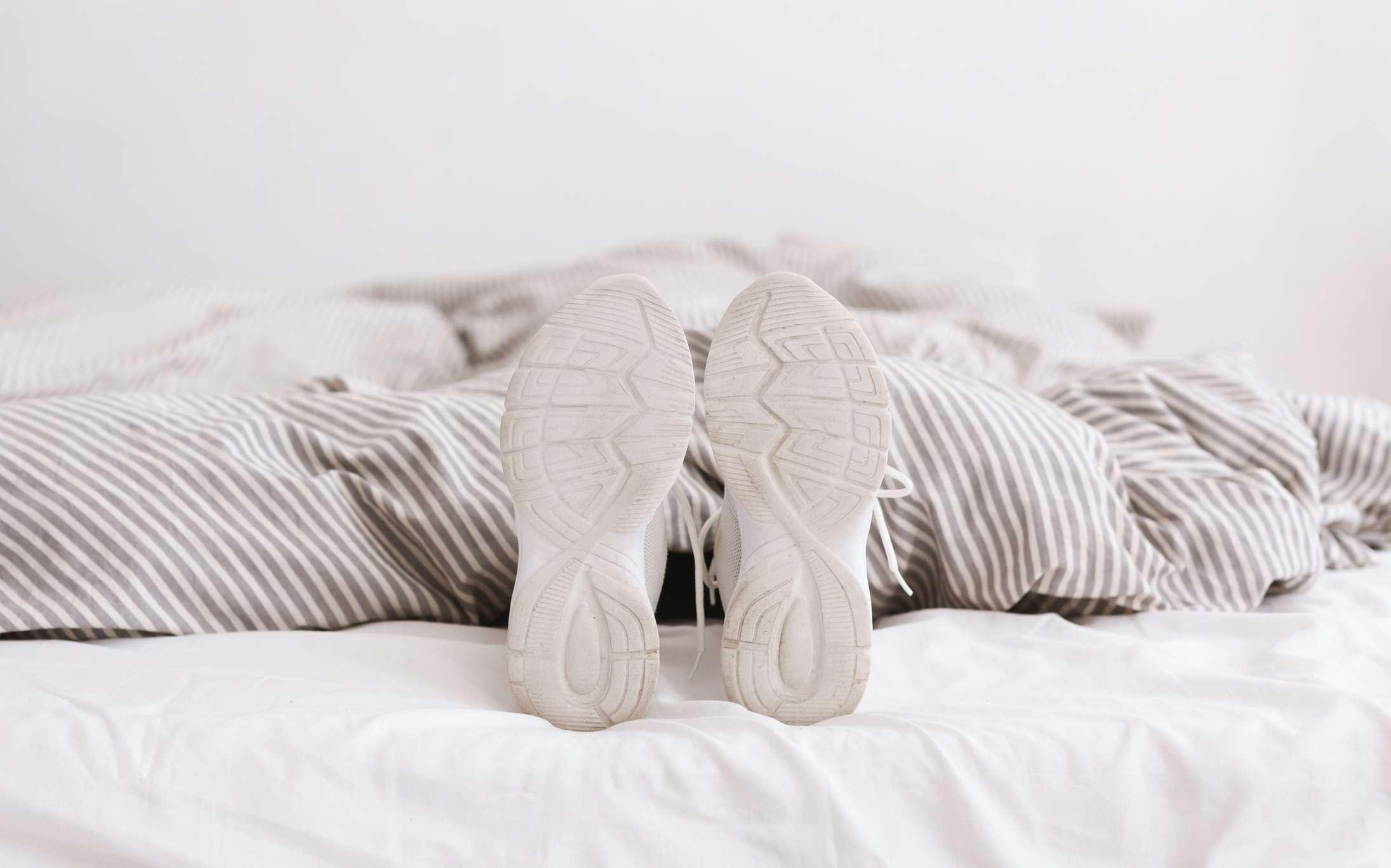 Junge, weibliche Beine in weißen Turnschuhen, am Bett liegend