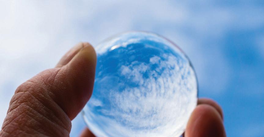 Die Hand eines Psoriasis-Patienten hält eine Glaskugel, in der sich ein blauer Himmel mit Wolken spiegelt. Ein Symbol der Hoffnung auf Genesung. Internationaler Psoriasis-Tag.