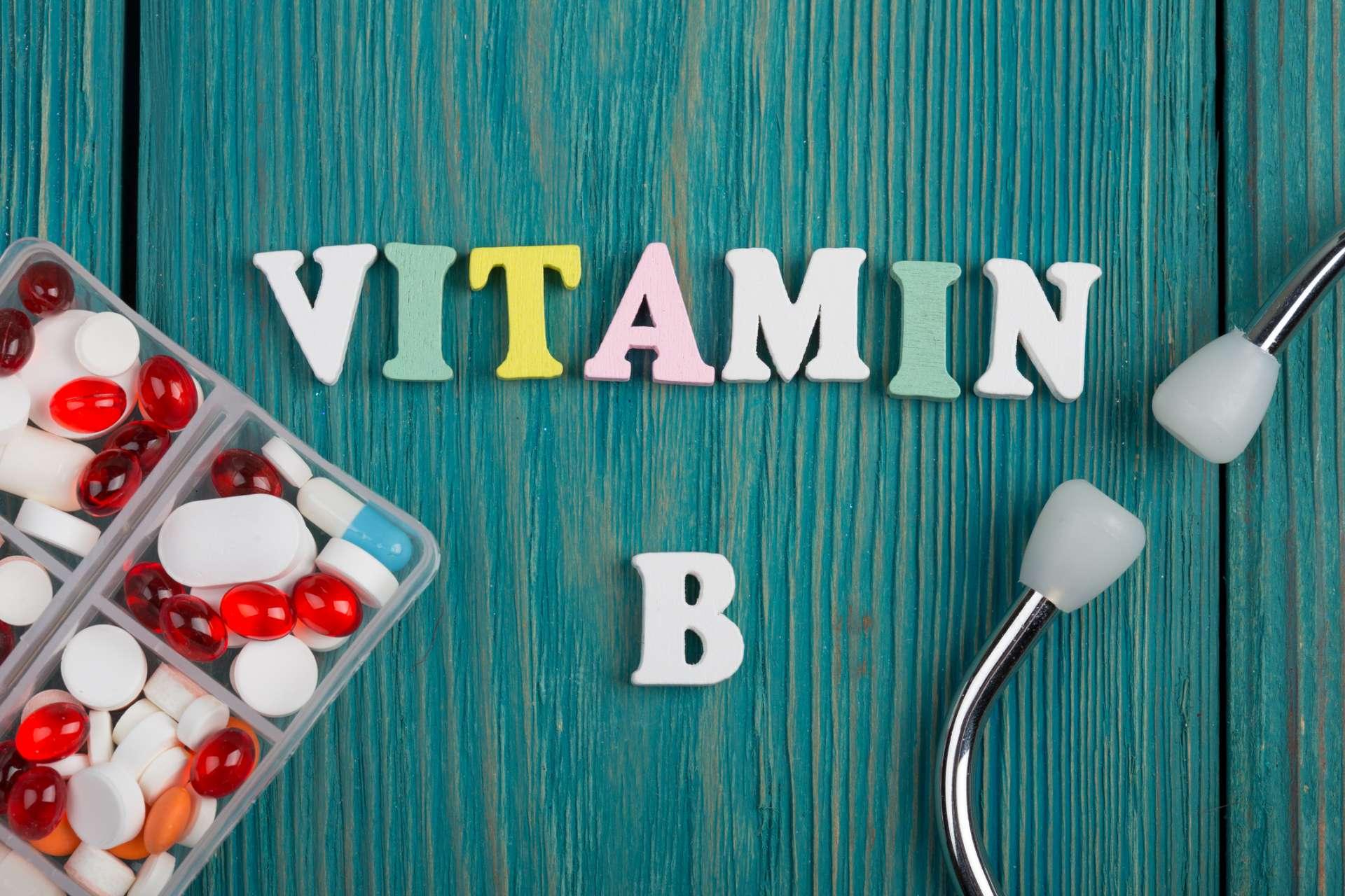 Text "Vitamin B" aus farbigen Holzbuchstaben, Stethoskop und Pillen auf blauem Holzhintergrund