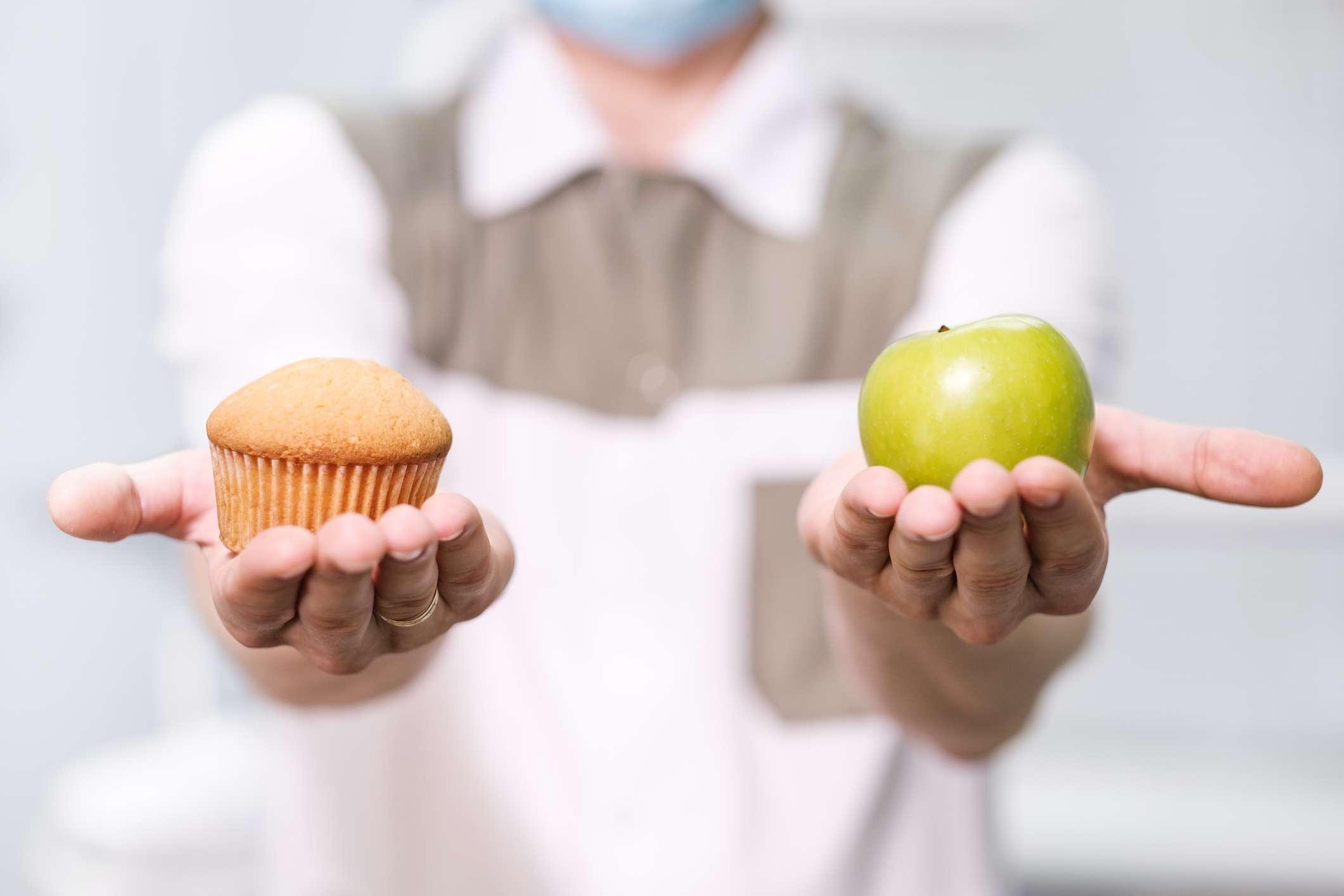 Doktor ein Zahnarzt ein Mann hält einen grünen Apfel und einen süßen Cupcake und zeigt auf der Waage eine Auswahl von nützlich gegen schädlich