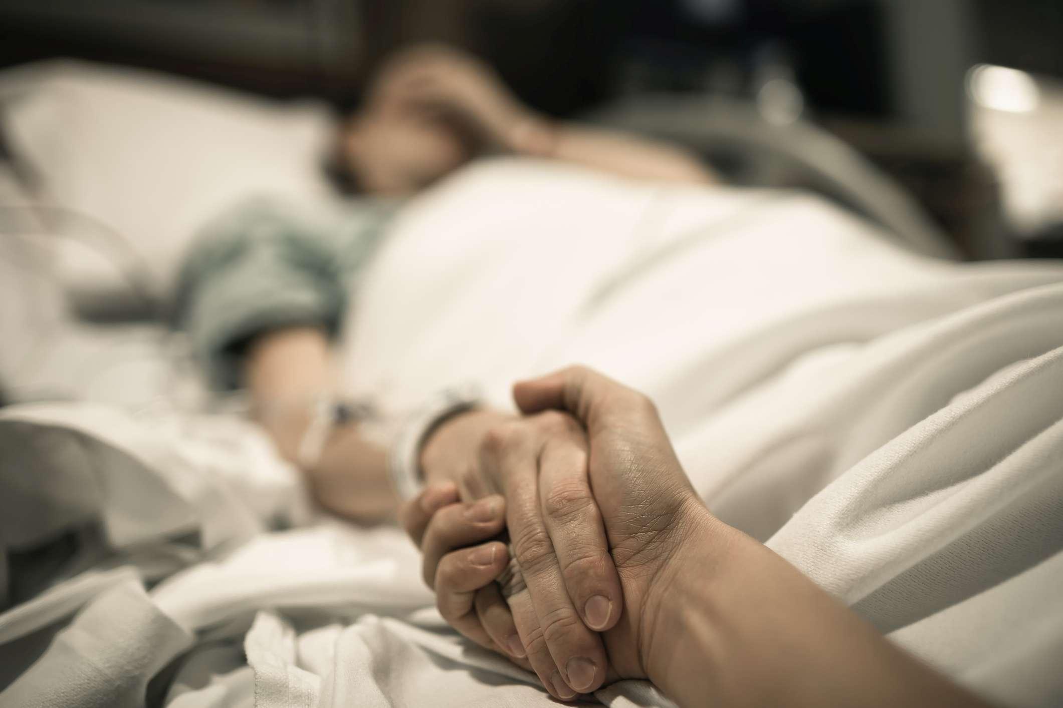 Kranke Frau, die im Krankenhausbett mit der Hand liegt, die von der Liebe eins gehalten wird. Familienlinien und medizinisches Tragödienkonzept.