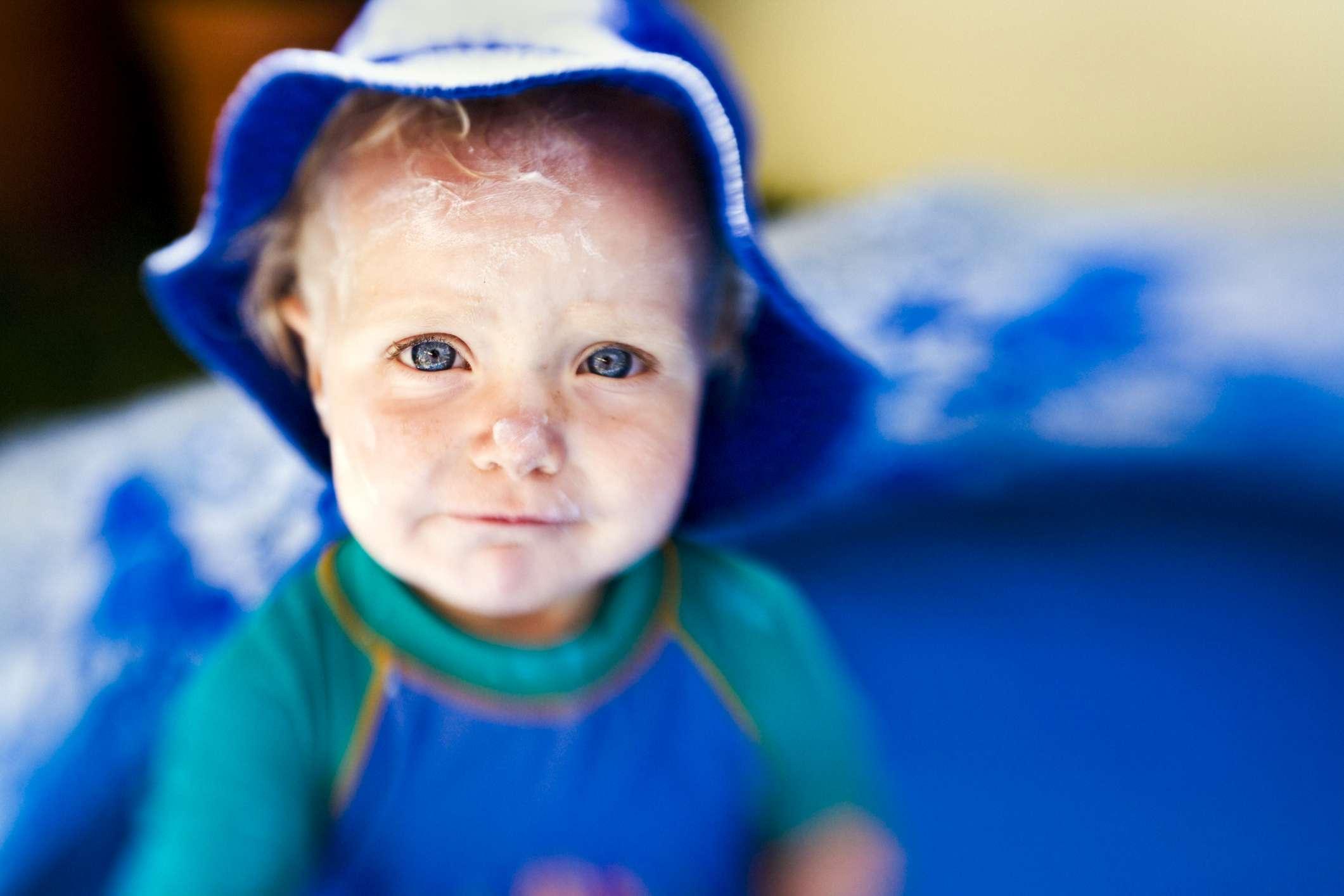 Sonnenschutz. Einjähriges Mädchen in einem Planschbecken, Gesicht mit Sonnencreme bedeckt und einen Hut und einen Sonnenbrandanzug tragend.