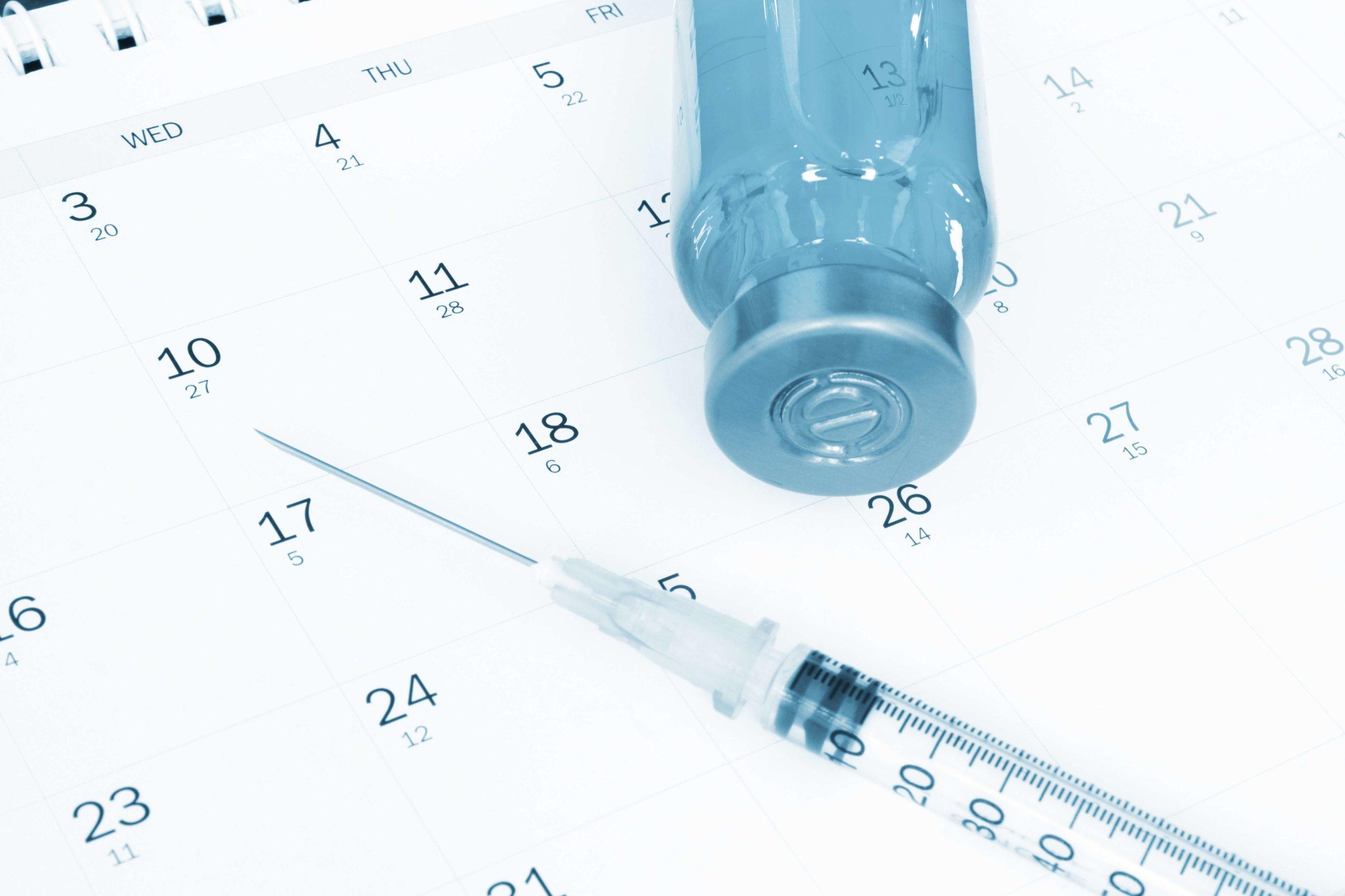 Impfstoff und Spritze auf Kalender.