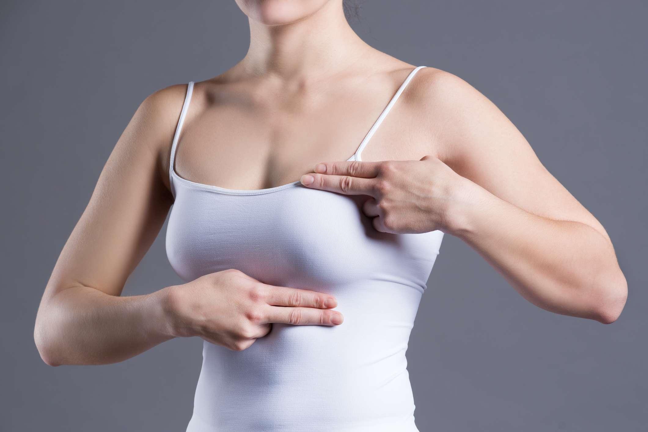 Brusttest, Frau untersucht ihre Brüste auf Krebs, Herzinfarkt, Schmerzen im menschlichen Körper auf grauem Hintergrund