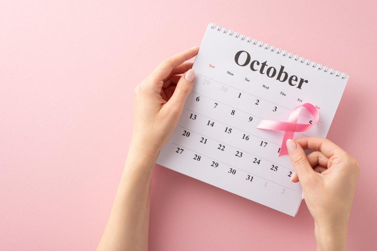 My Breast Cancer awareness setup. First person top view of girl&#8217;s hands holding October calendar with pink ribbon, gearing up for doctor&#8217;s visit on pastel pink background with blank area for text