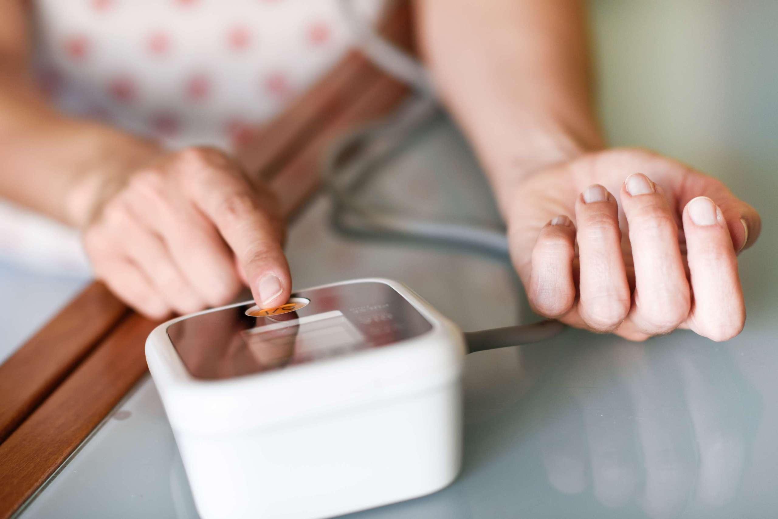 Frau mittleren Alters, die ihren eigenen Blutdruck mit einem elektronischen Blutdruckmessgerät zu Hause misst